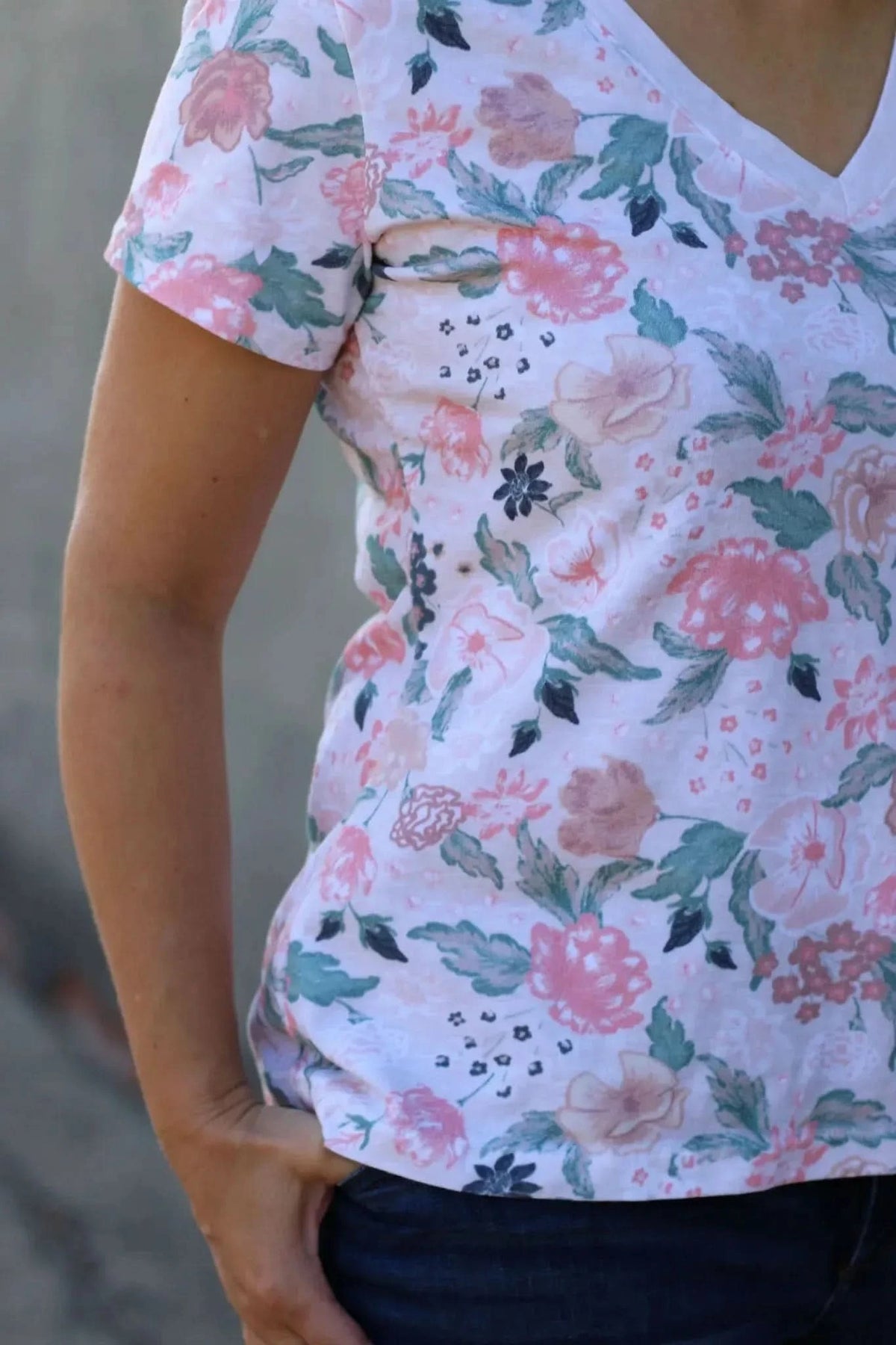 A person wears a white floral top with pink, green, and blue flowers.