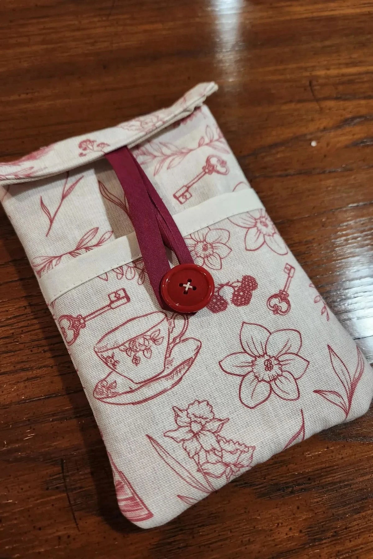 Red fabric with printed tea cups, keys, and floral toile pattern.