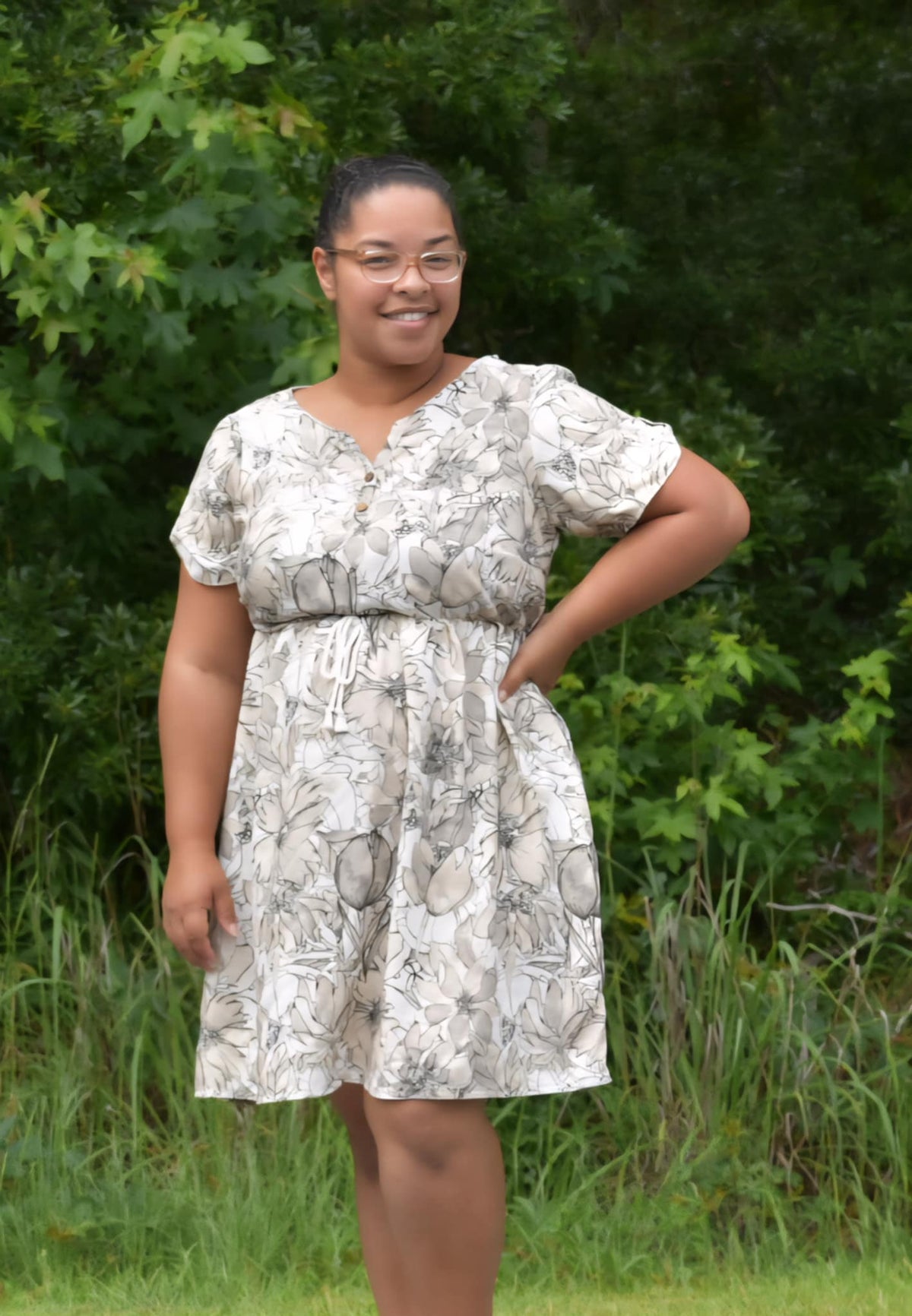 A woman in a sepia sketch floral dress smiles with her hand on her hip.