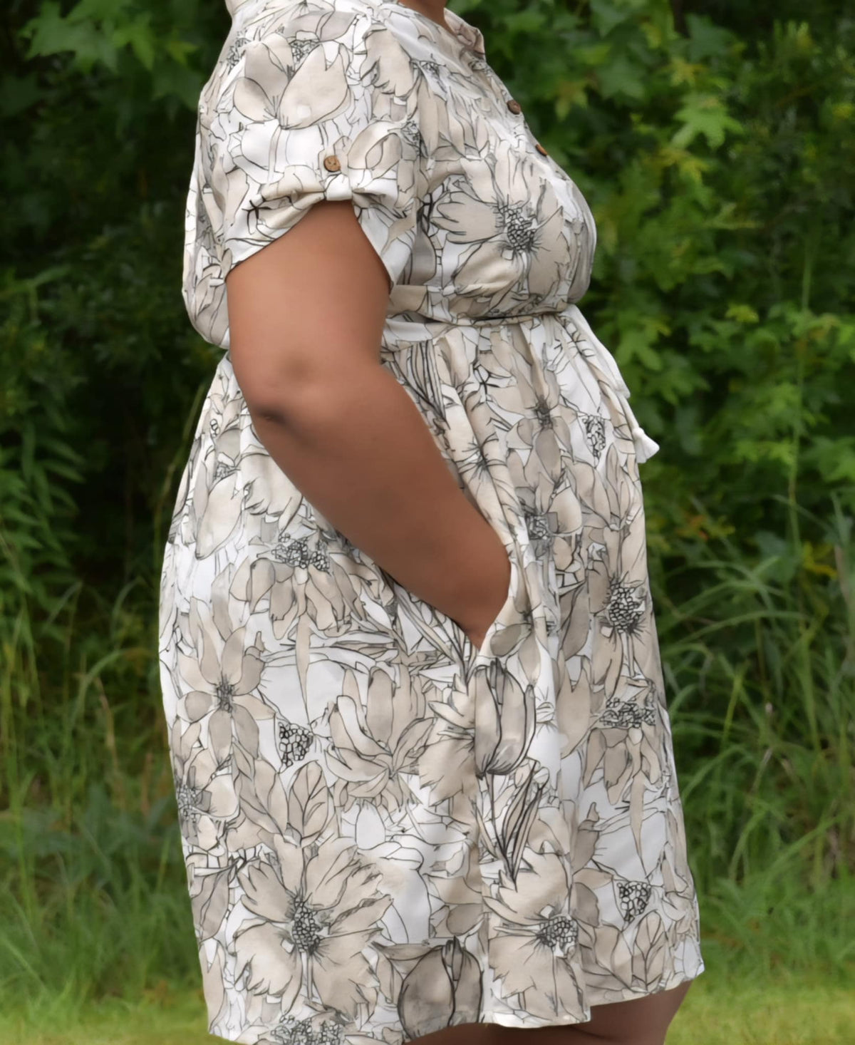A person wearing a sepia sketch floral dress with pockets.