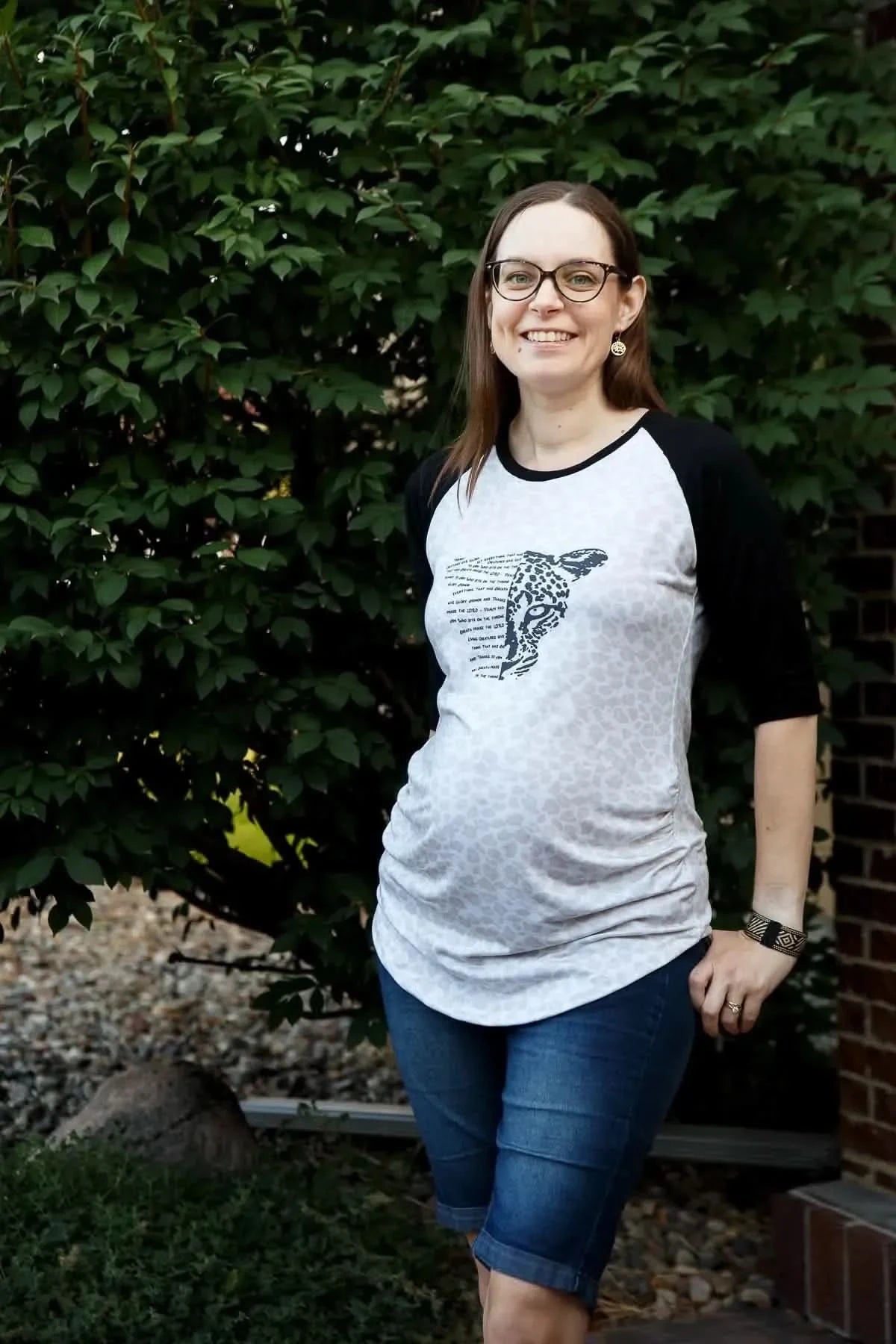 Woman modeling gray raglan T-shirt with Creatures Give Glory faith panel print, paired with denim shorts.