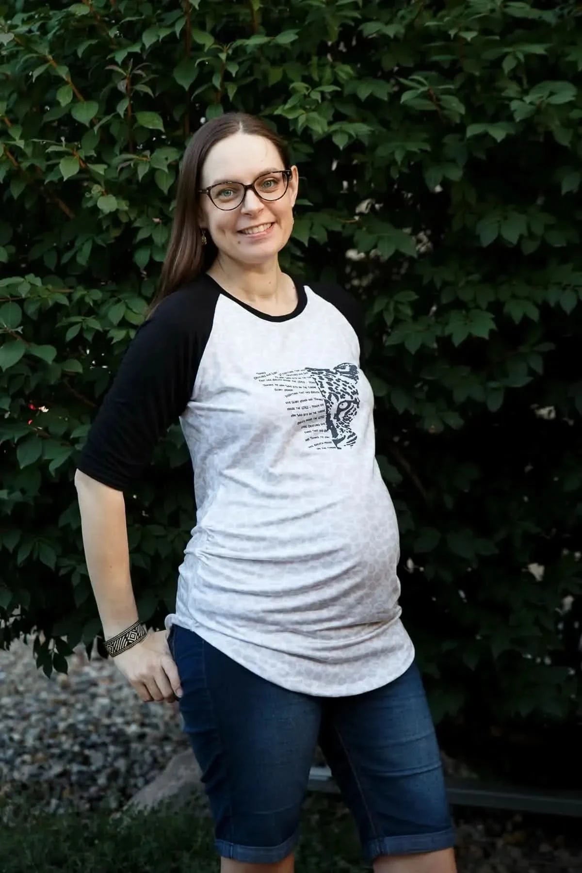 Pregnant woman in gray raglan T-shirt with Creatures Give Glory panel design.