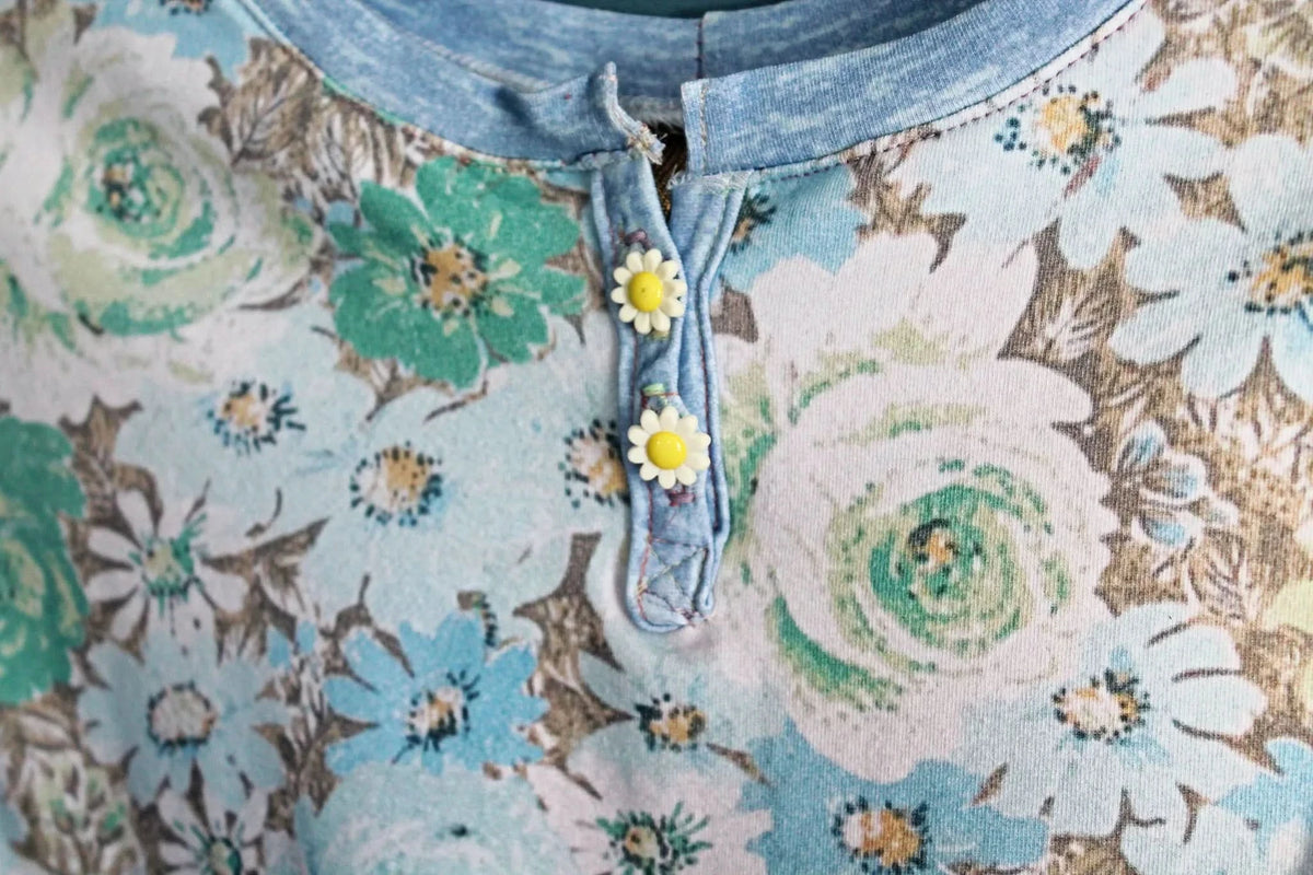 A floral print fabric with blue, green, and white flowers, featuring two daisy buttons.