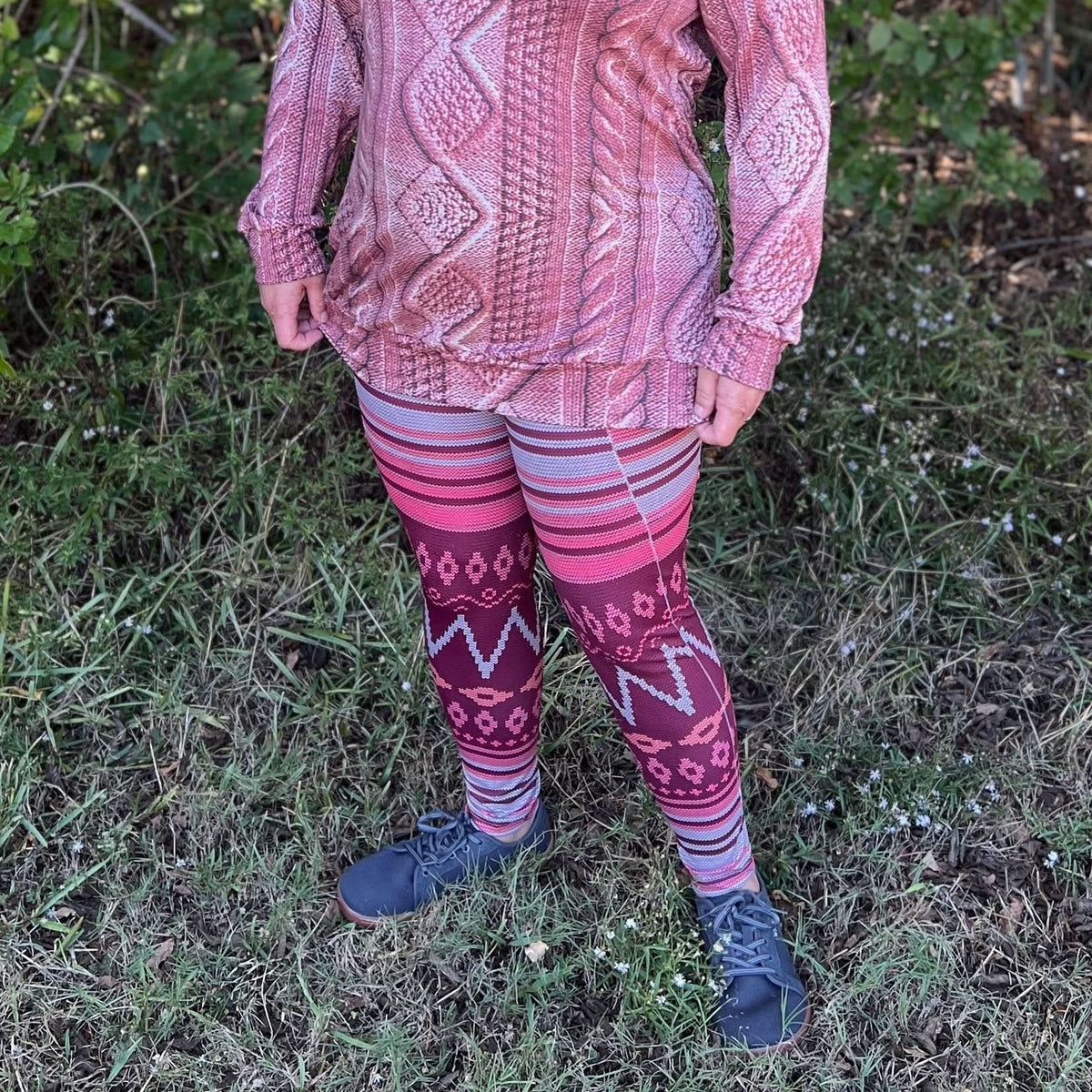 A person wearing a pink cable knit top and patterned leggings stands on grass.
