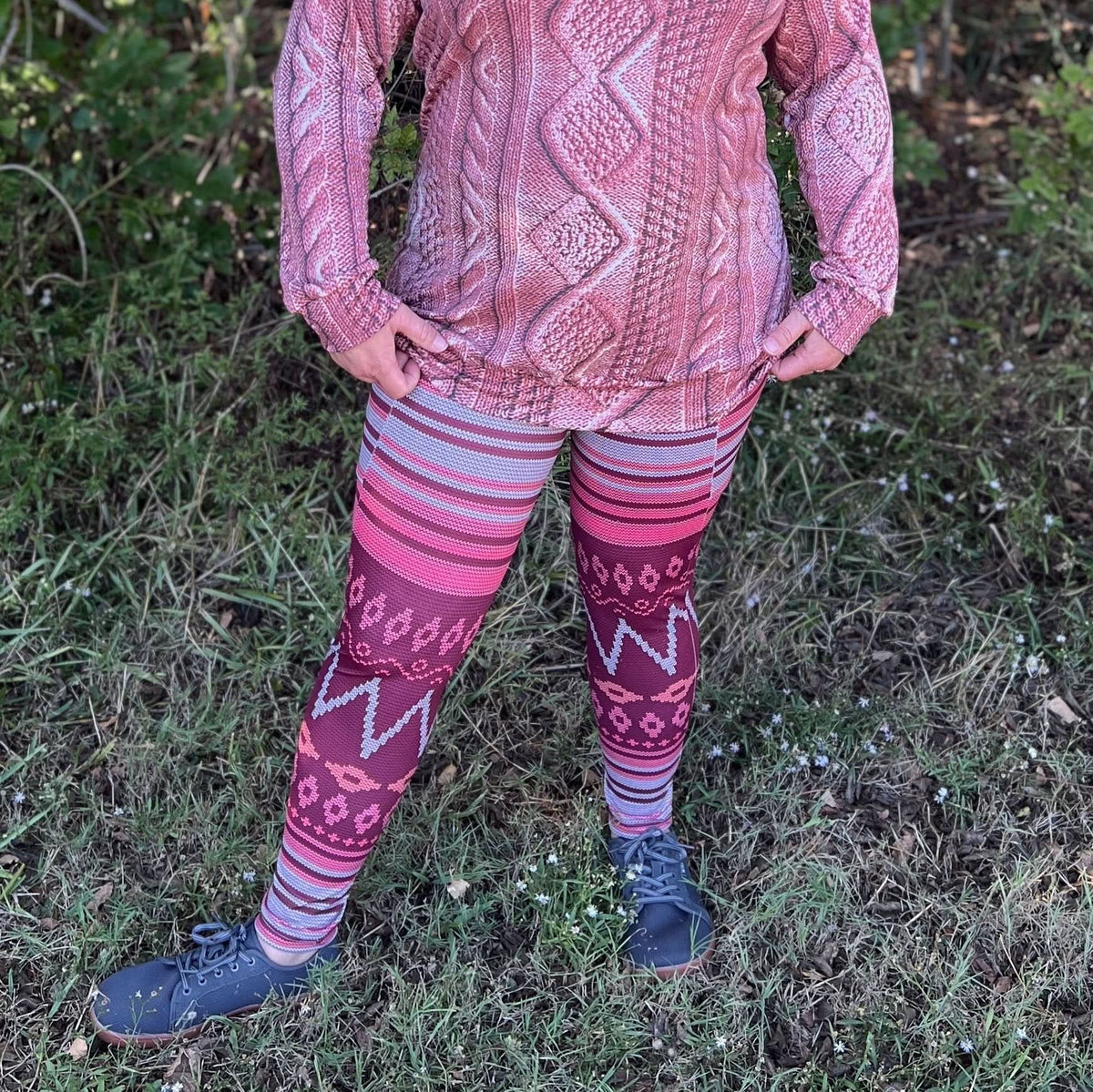 A person wears a pink sweater and patterned leggings with dark shoes.