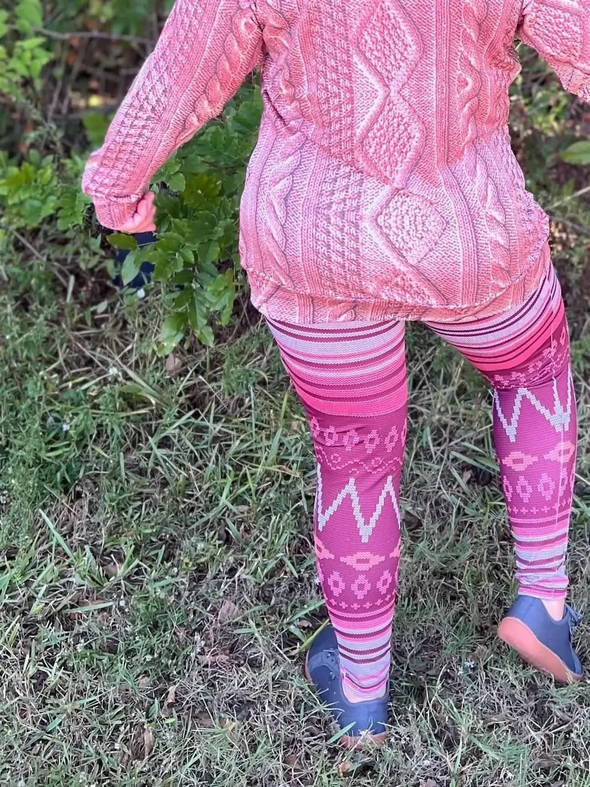 Rear view of pink abstract patterned leggings on a model in grass.