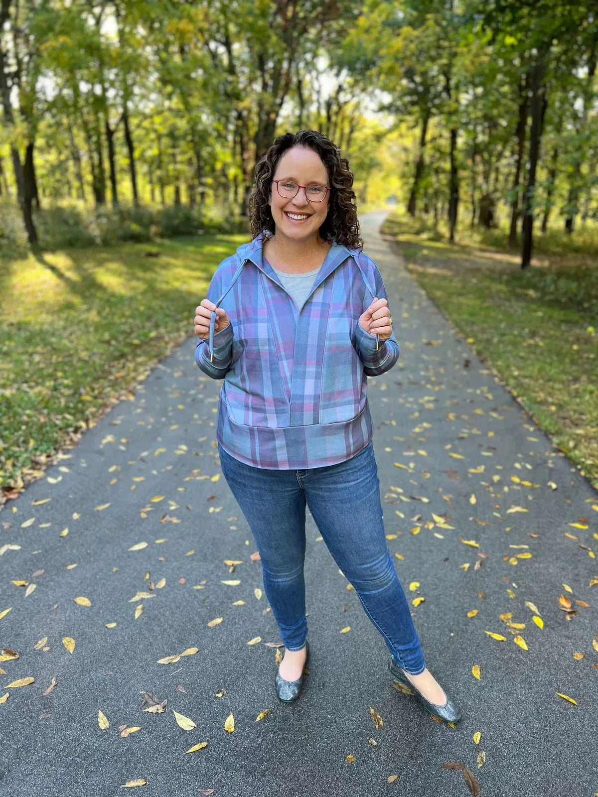 Woman wearing a dark plaid shirt in green and pink on a wooded path.