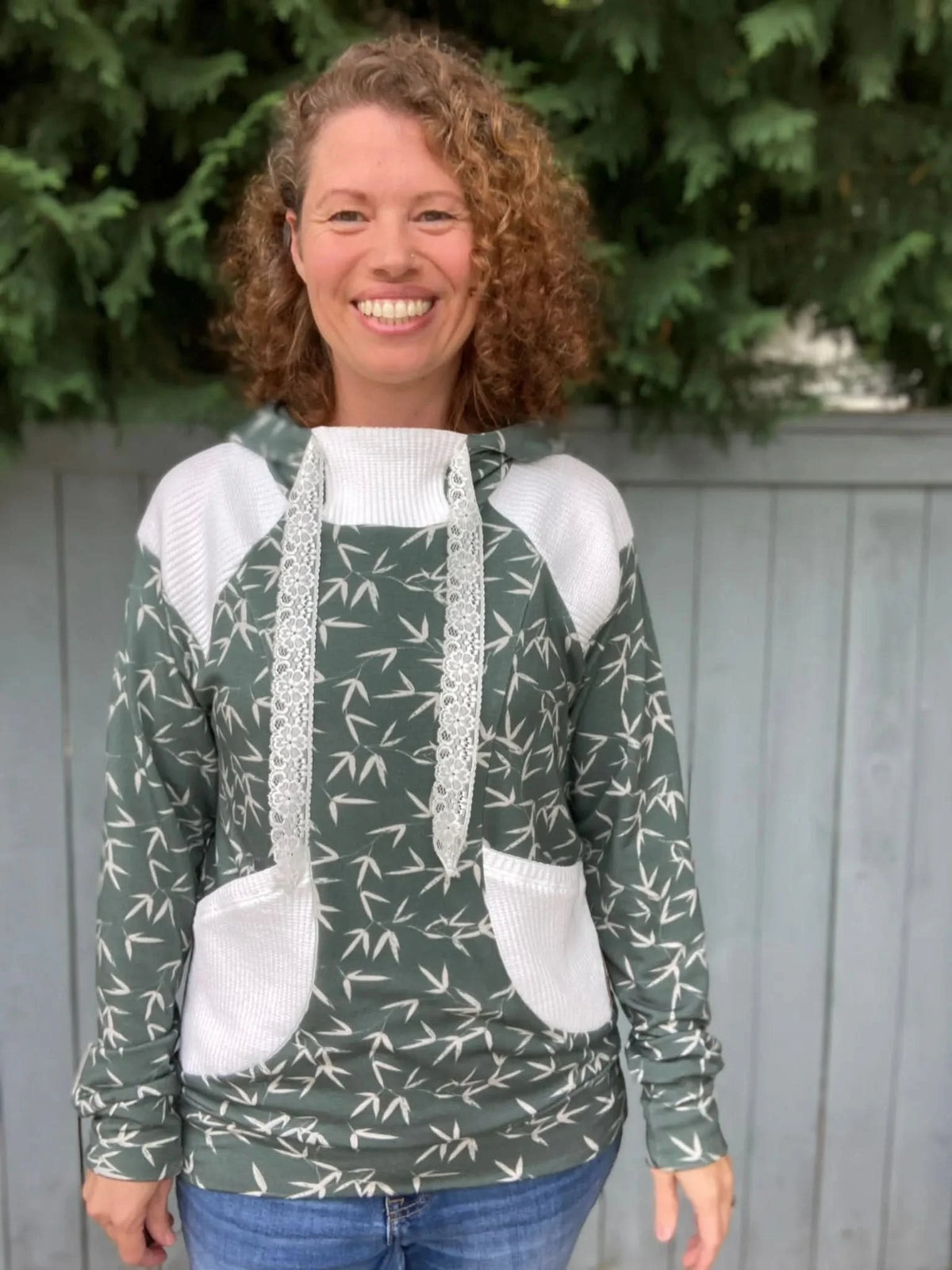 Woman wearing a green hoodie with white accents and bamboo leaf print, standing outdoors.