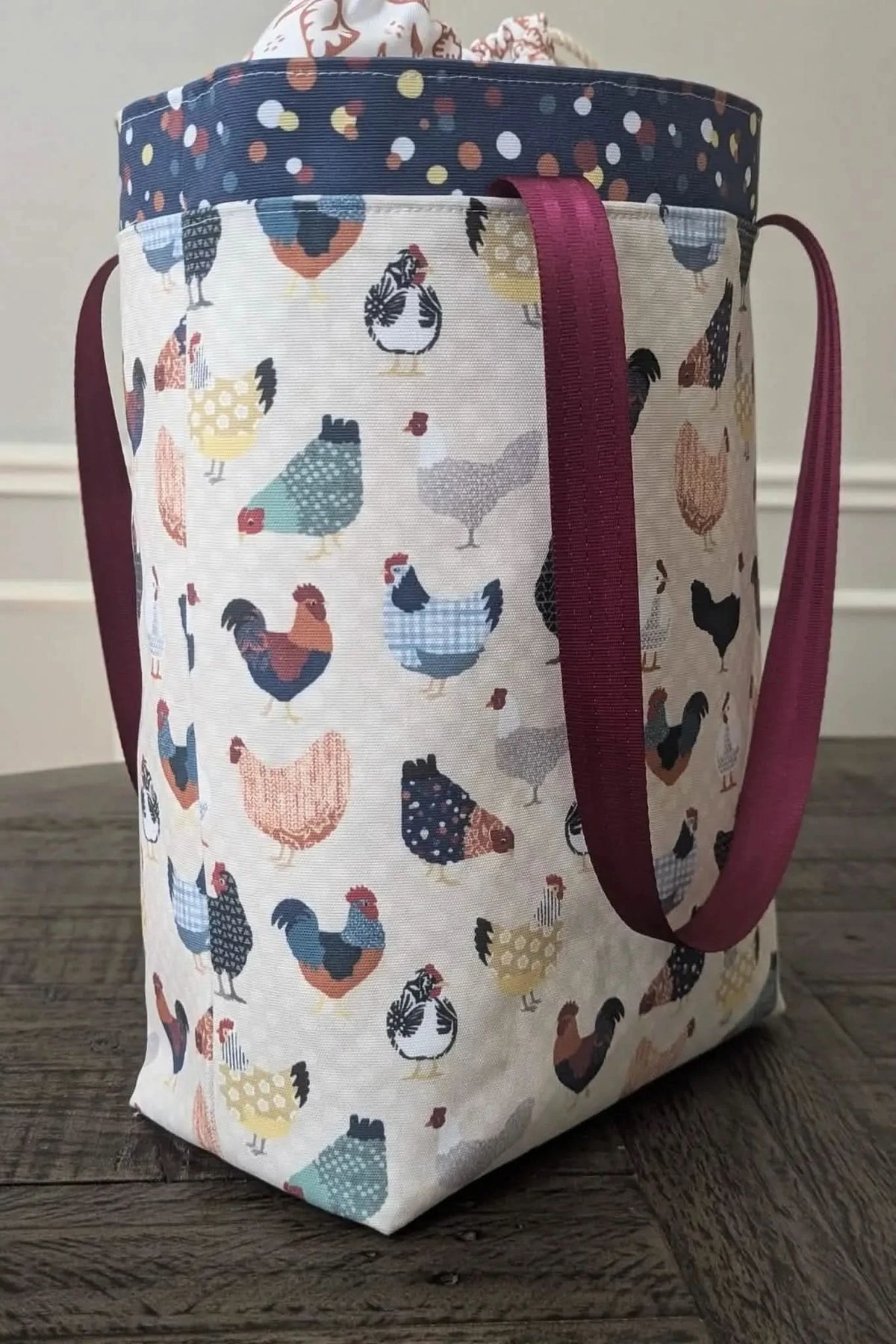White fabric with colorful patchwork chicken print, shown as a tote bag with purple handles.