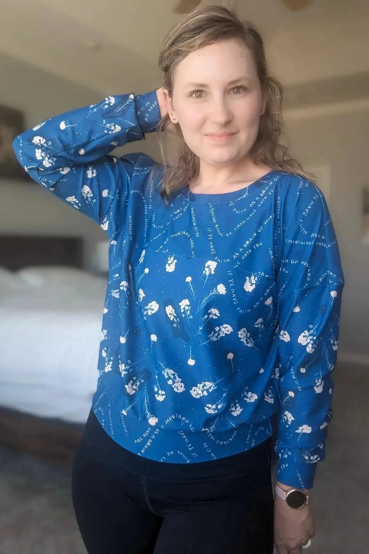 A woman wears a blue long-sleeved shirt with white floral and text patterns.