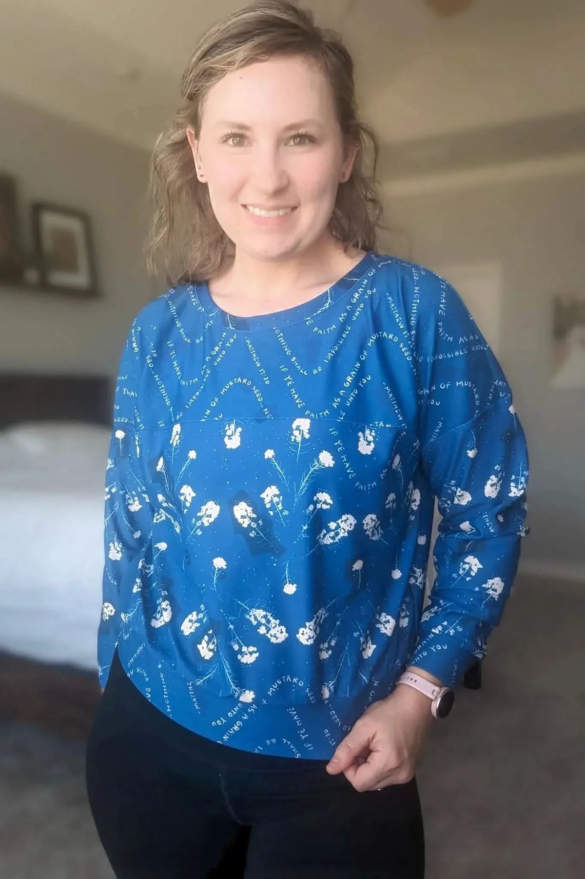 A woman wears a blue long-sleeved shirt with white floral and text patterns.