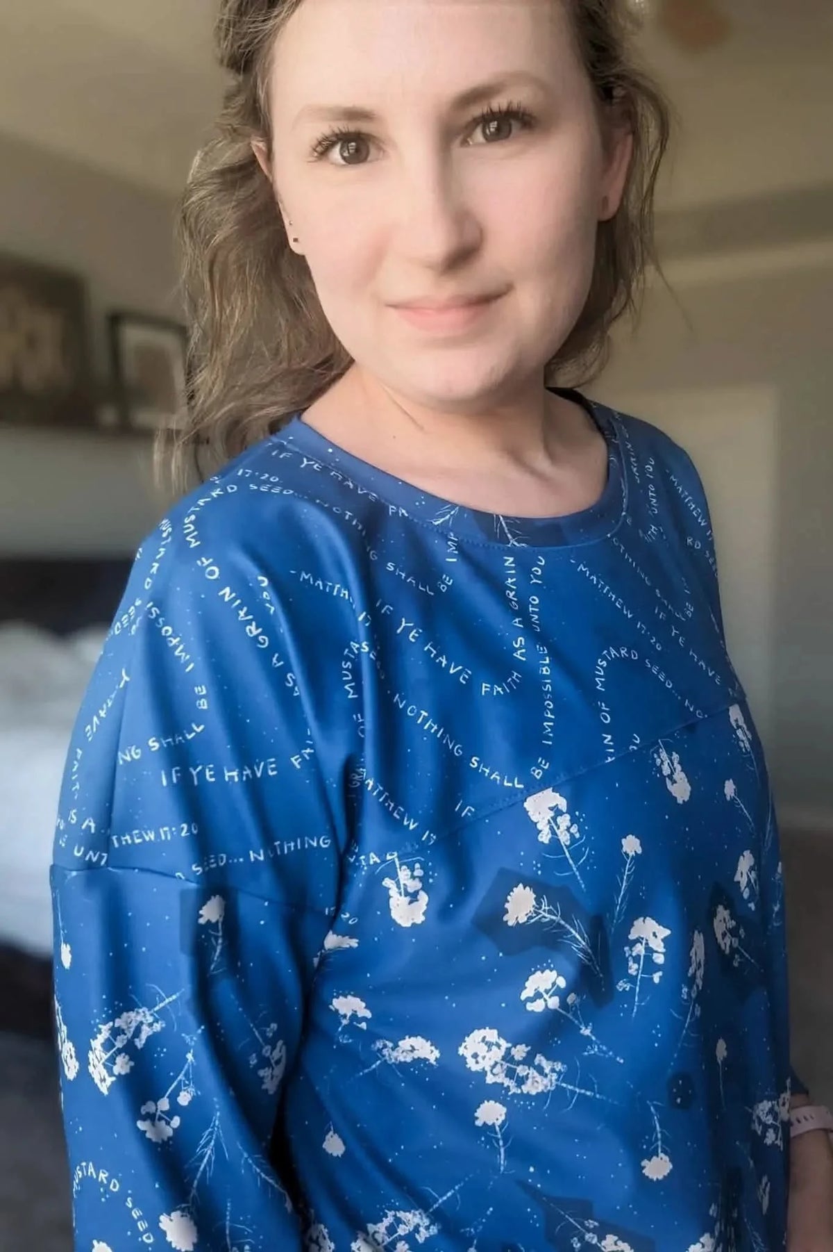A woman wears a blue shirt with white text and floral patterns.