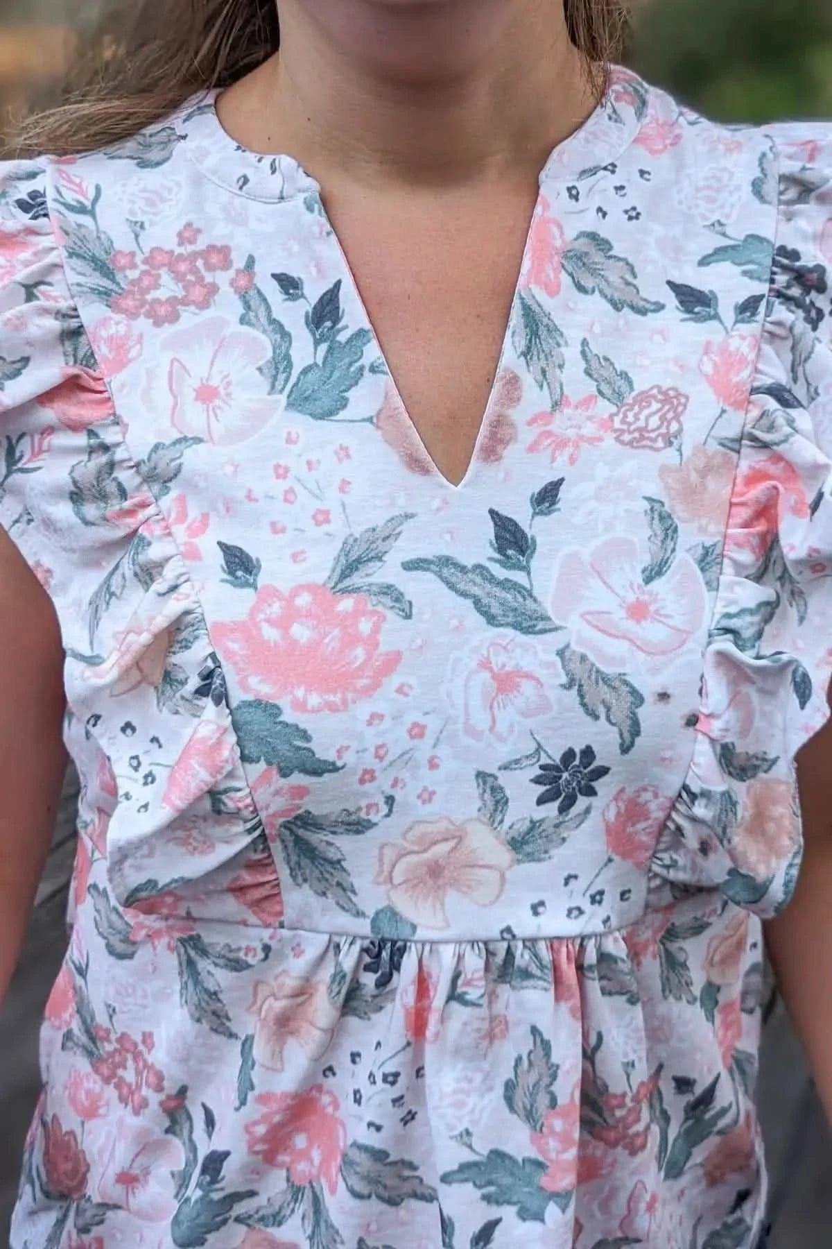 A person wearing a white top with a blush floral print and ruffled sleeves.
