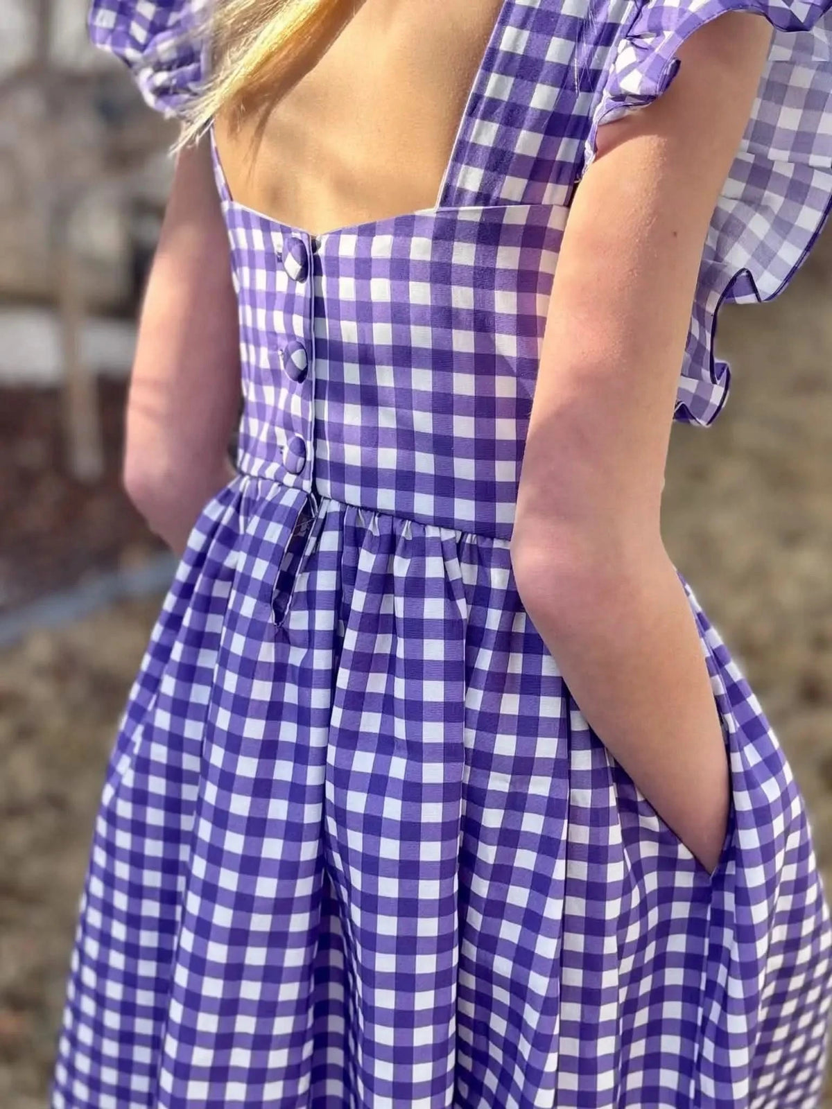A person wearing a violet and white gingham dress with buttons and pockets.
