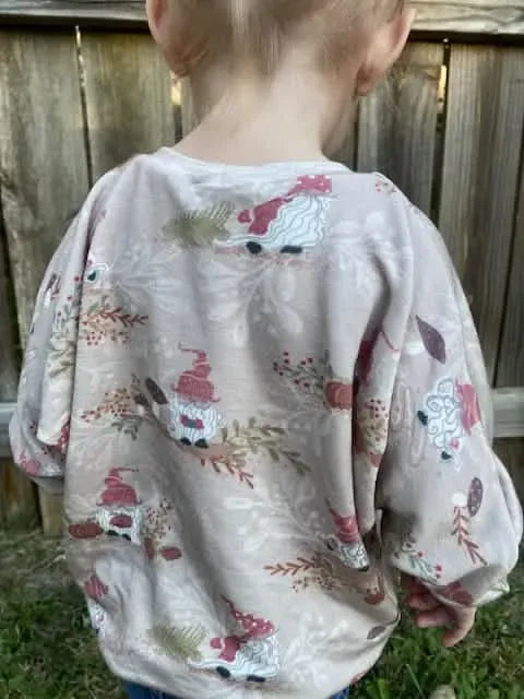 Child wearing a tan shirt with an autumn gnome print.