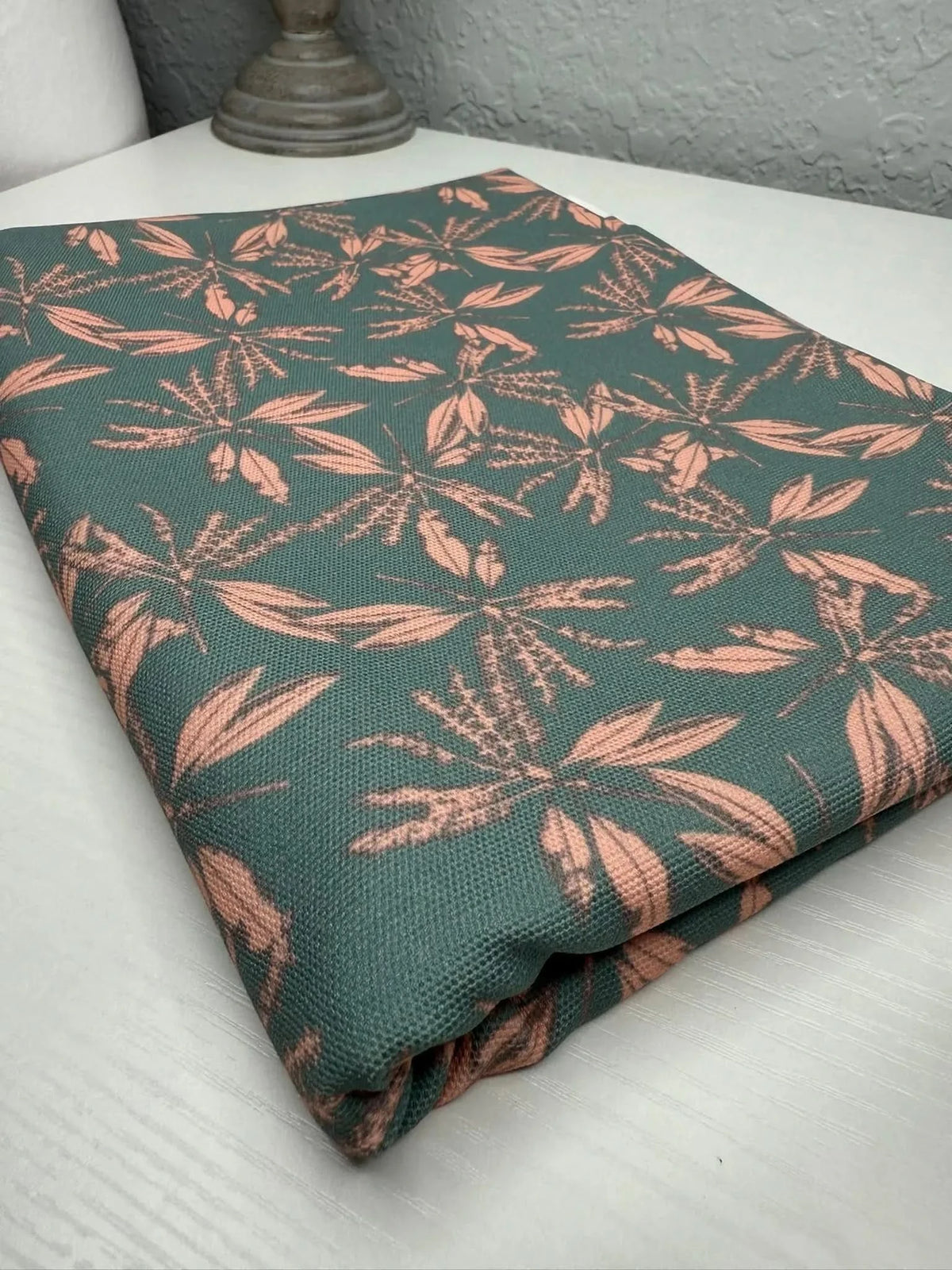 Blush hollow floral print fabric with green and pink leaf motifs on a folded teal base.