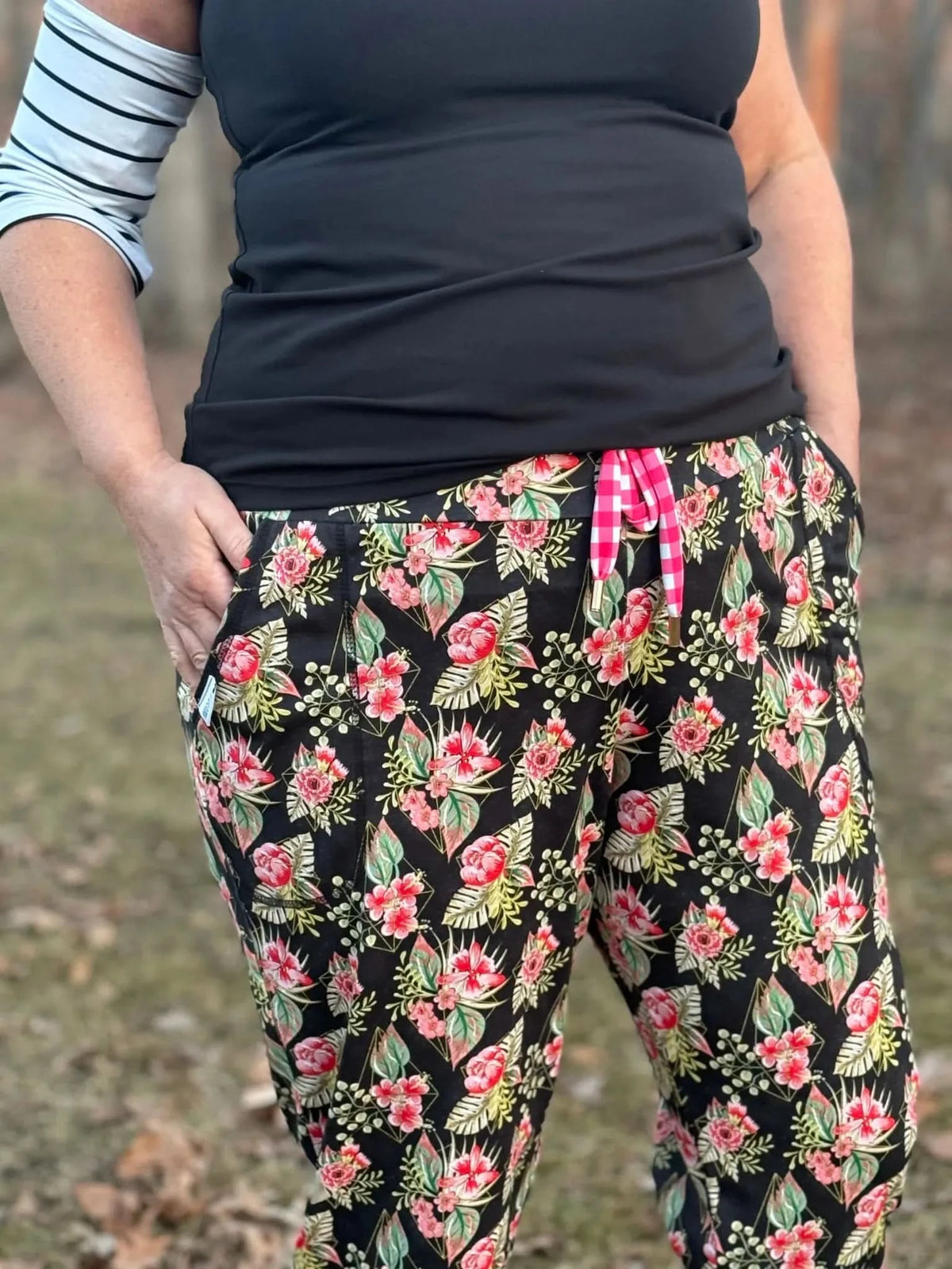 Woman modeling black top and pink floral tropical print pants with green leaves outdoors.