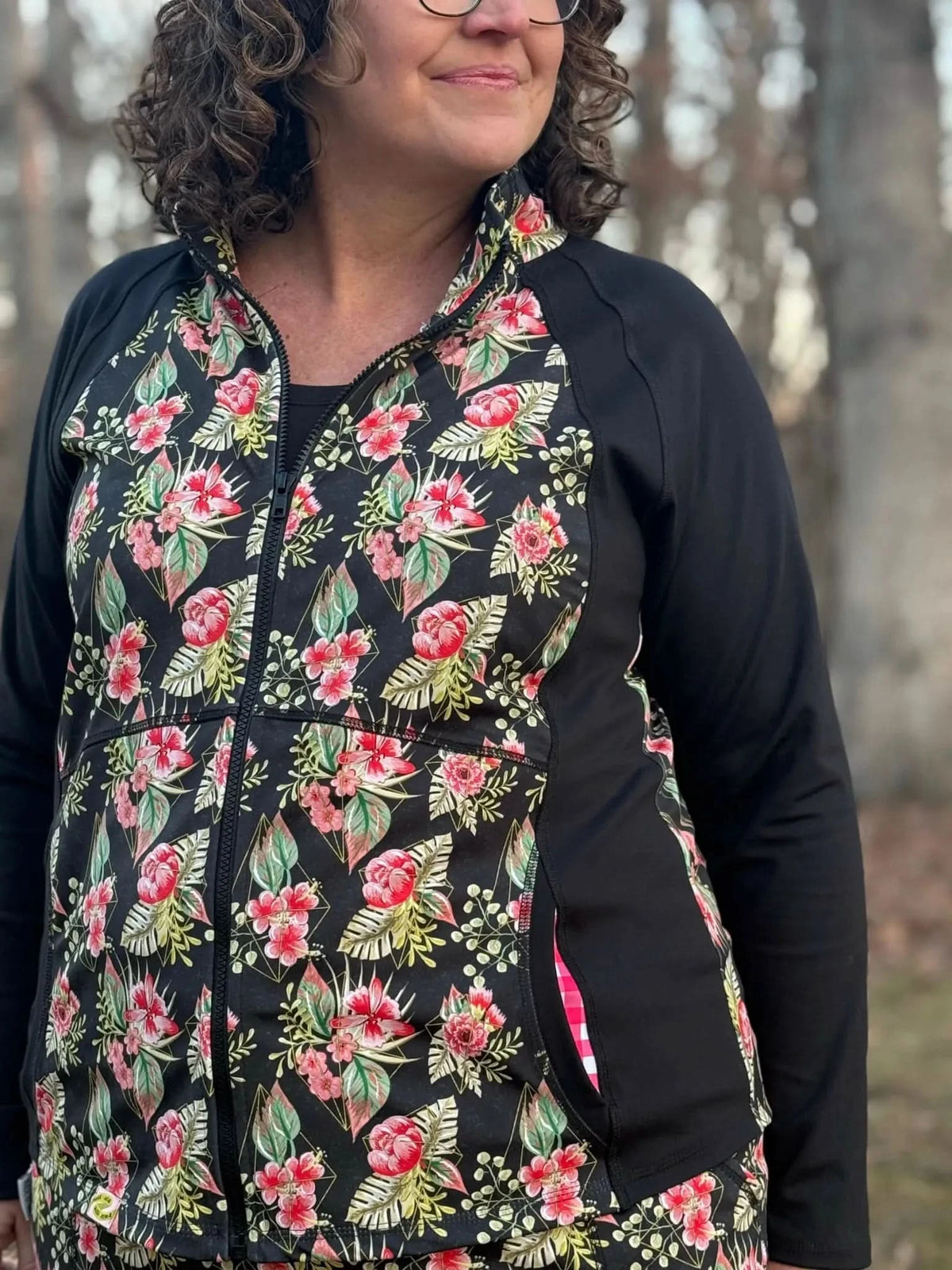 Floral tropical fabric with pink blooms and green leaves on a black background.