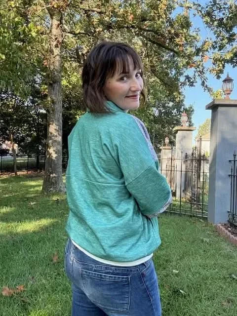 A woman wears a grass green heather long-sleeved top and blue jeans outdoors.