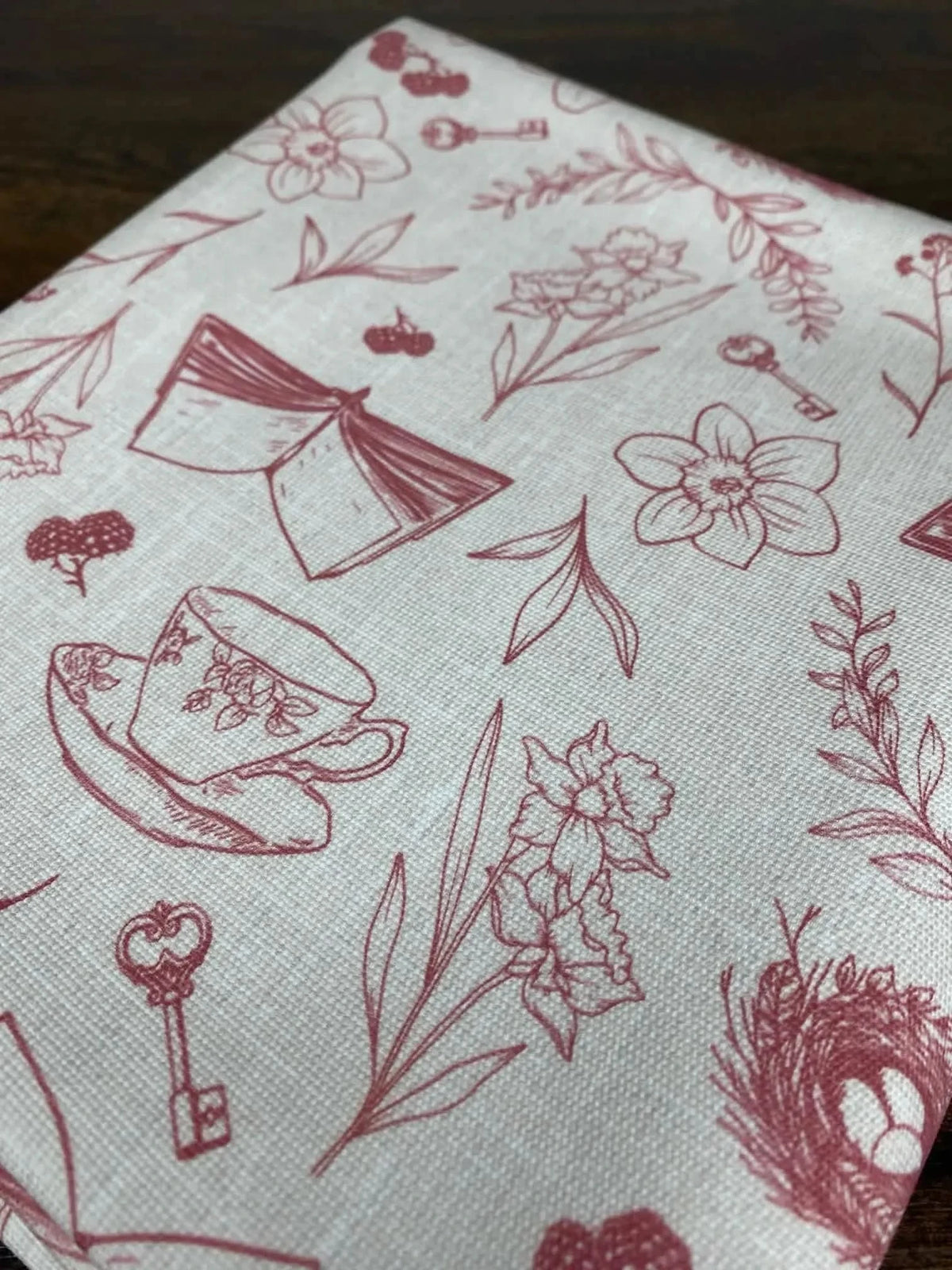 Red fabric with printed illustrations of teacups, books, keys, flowers, and berries.