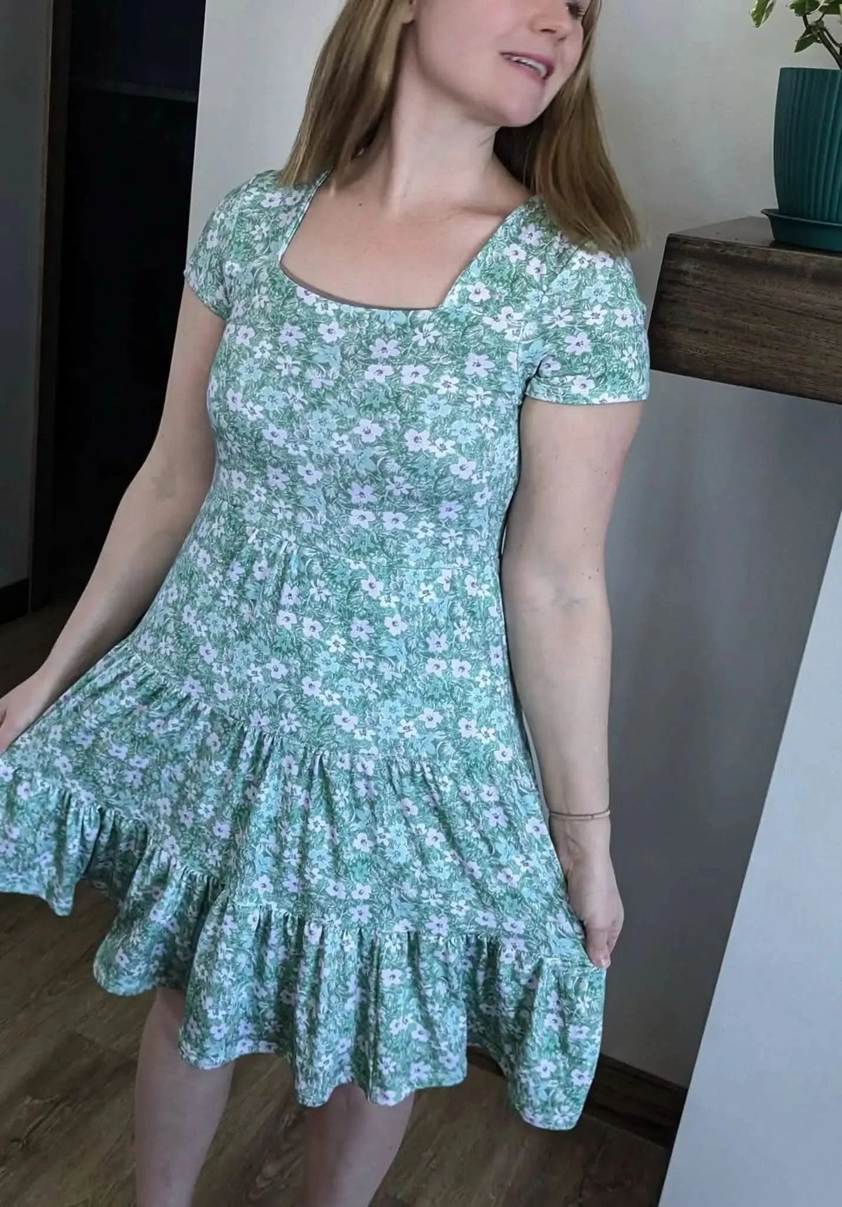 Woman wearing a green floral print dress with a square neckline and ruffled hem.