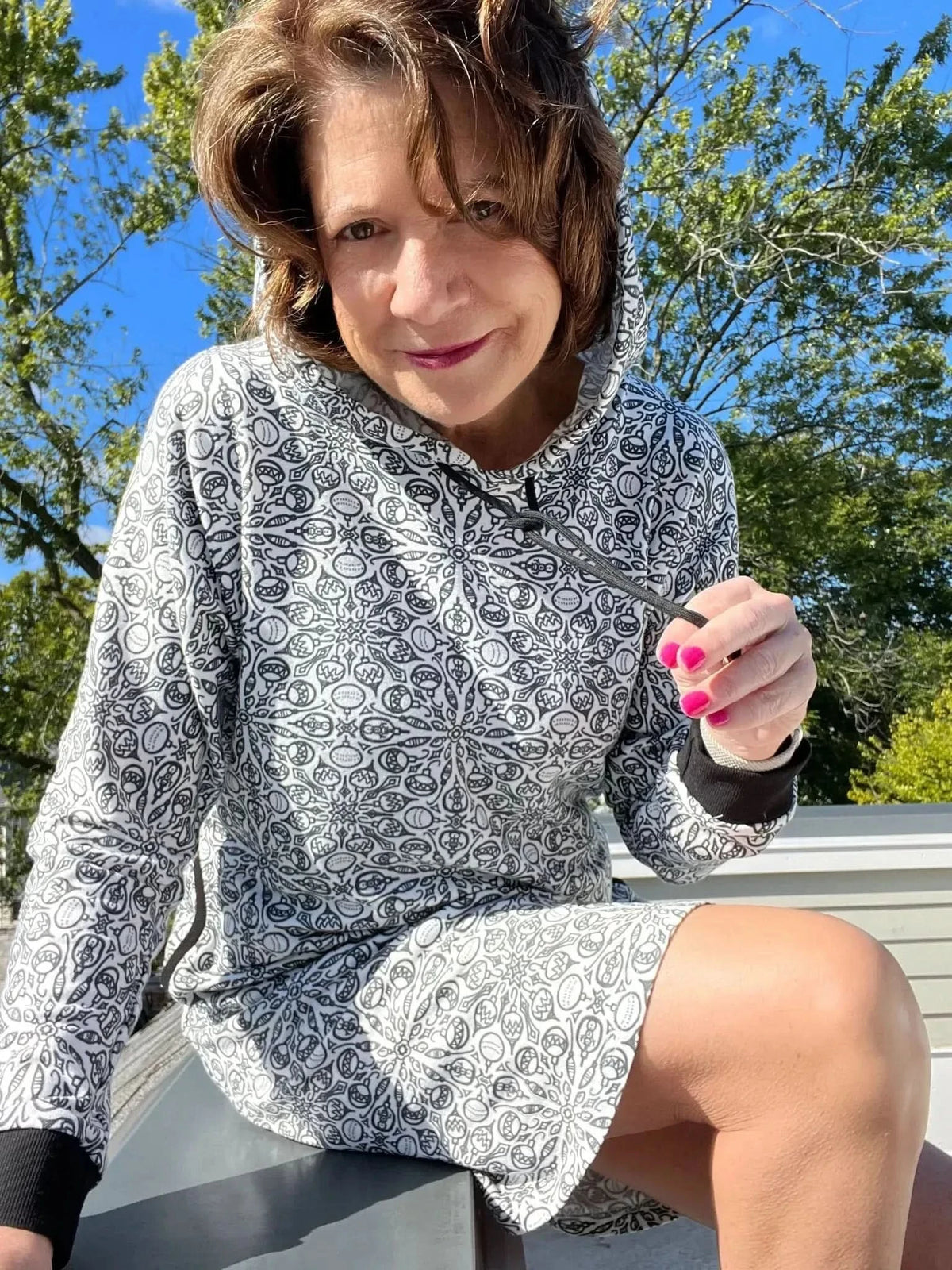 Woman modeling a gray hooded dress with intricate white floral print on outdoor steps.