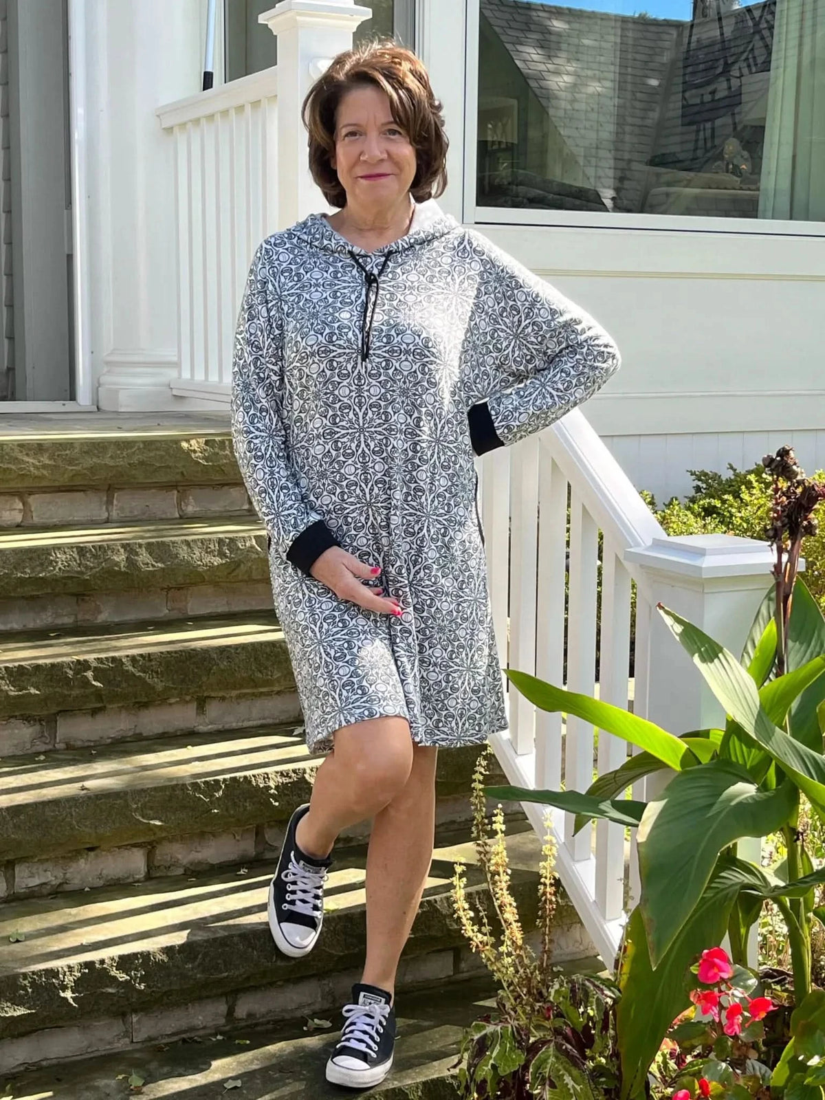 Woman modeling a gray patterned hoodie dress on front porch steps.