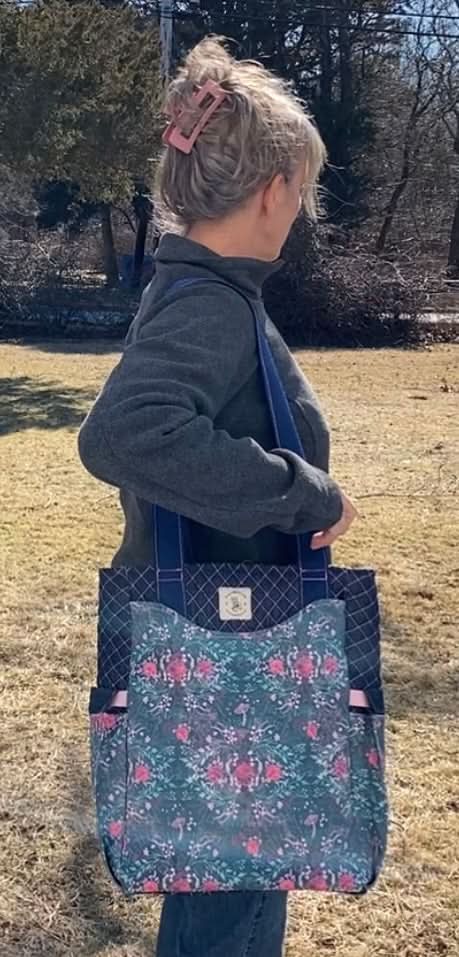A woman carries a tote bag with a dark floral and mushroom pattern.