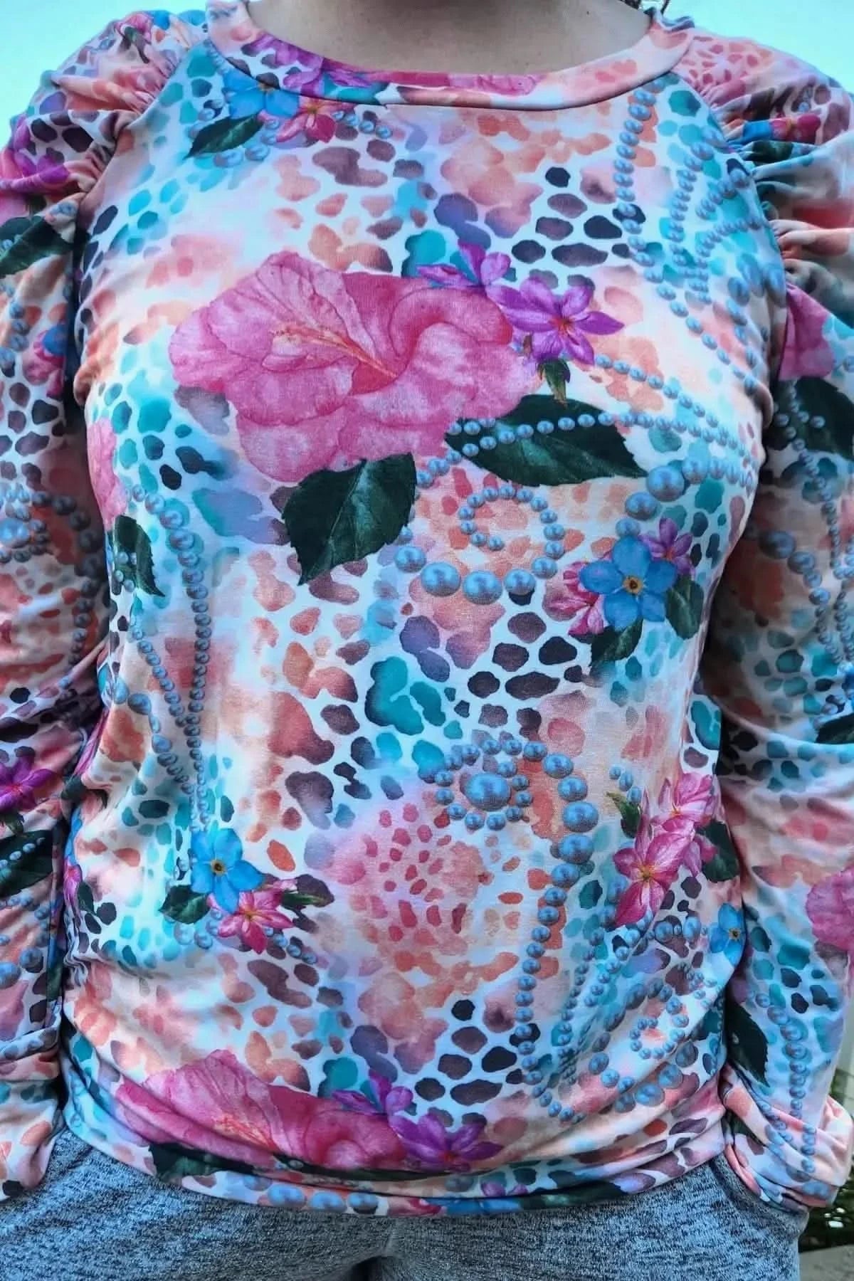 Vibrant tropical fabric with wild hibiscus flowers, pink blooms, green leaves, and blue accents on a textured background.