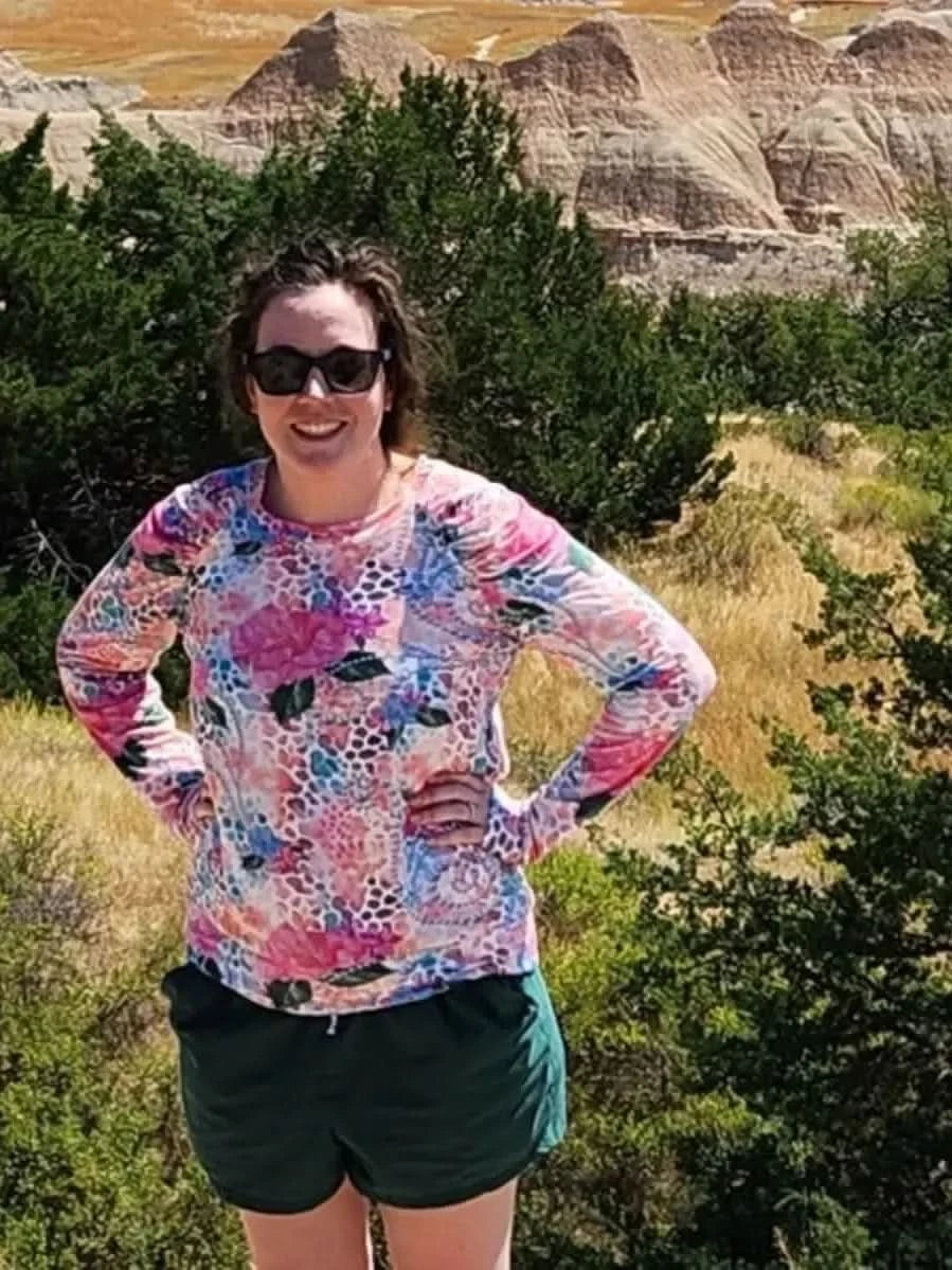 Woman wearing long-sleeve floral hibiscus print top and green shorts in scenic badlands.
