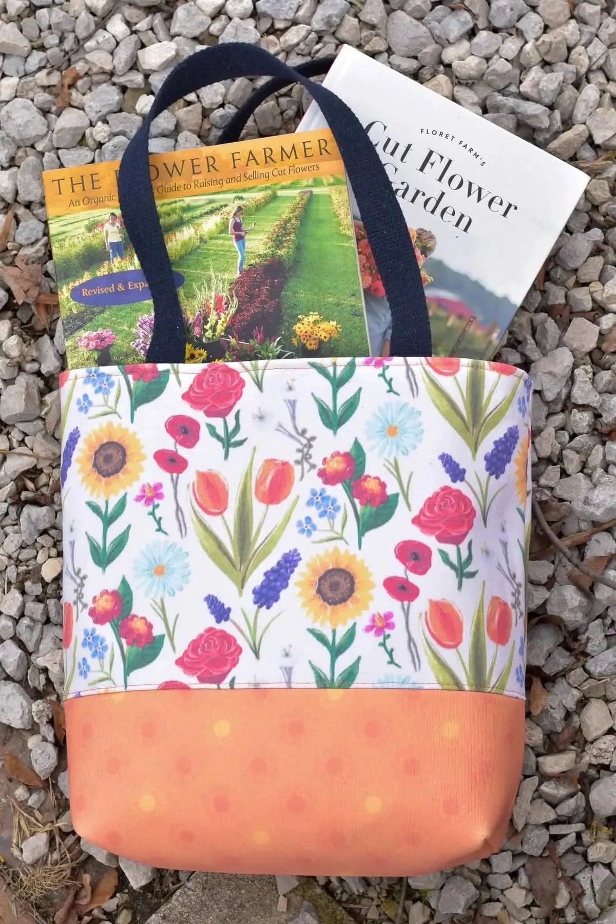 A tote bag with a vibrant floral print and an orange bottom, holding two gardening books.