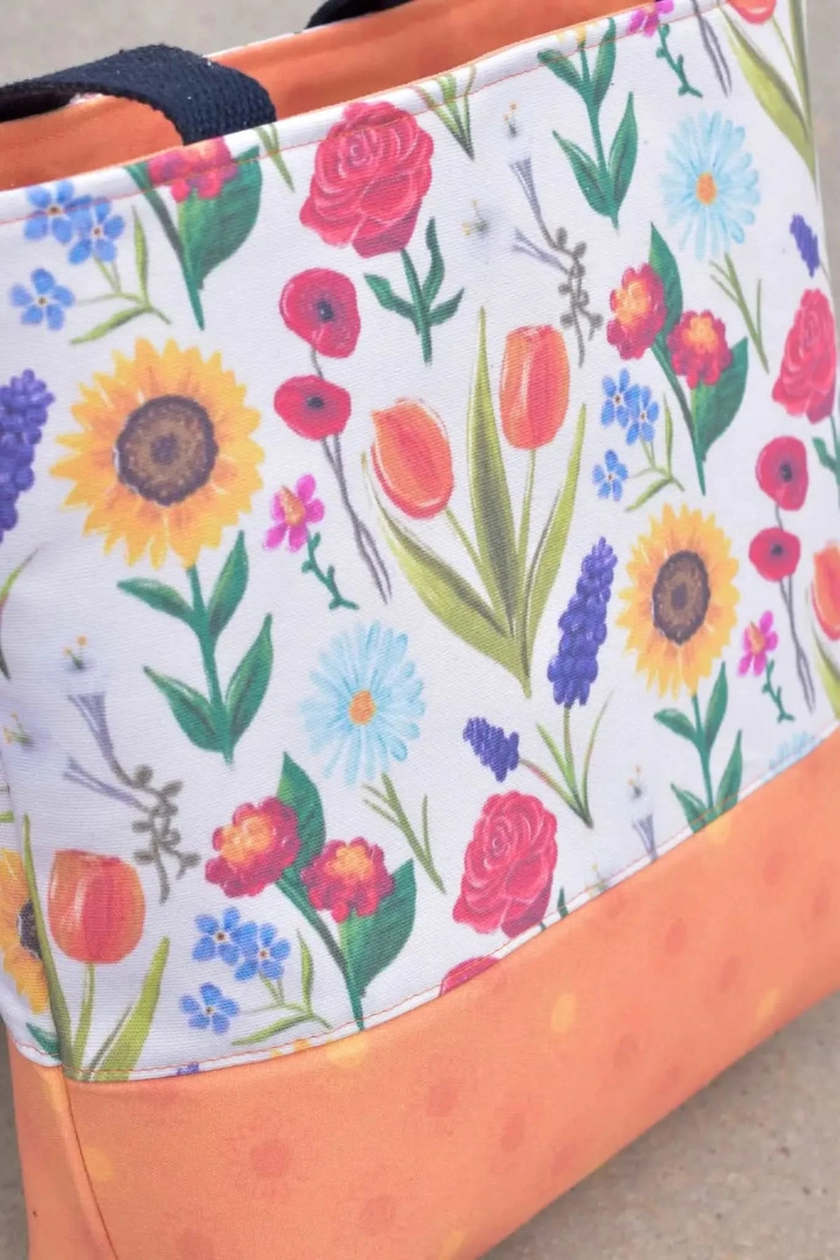 Vibrant orange fabric with botanical print of garden flowers, sunflowers, roses, and tulips.