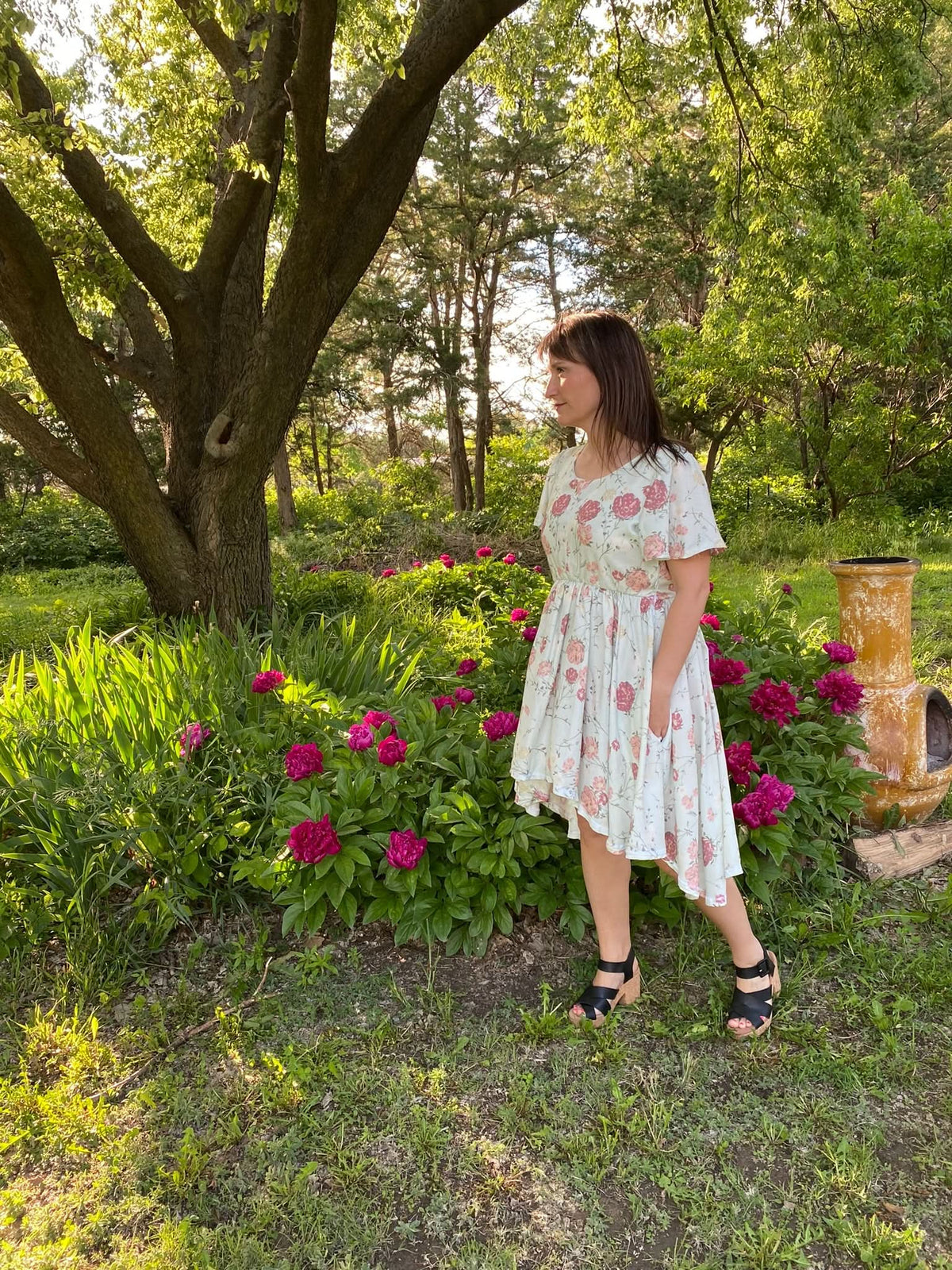 Woman in a floral dress with an asymmetrical hem and black wedge sandals.