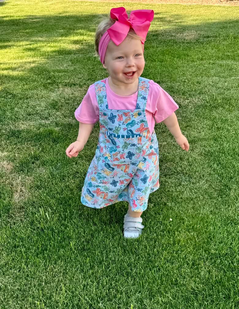 A child wears a dress with a painted butterfly pattern over a pink shirt.