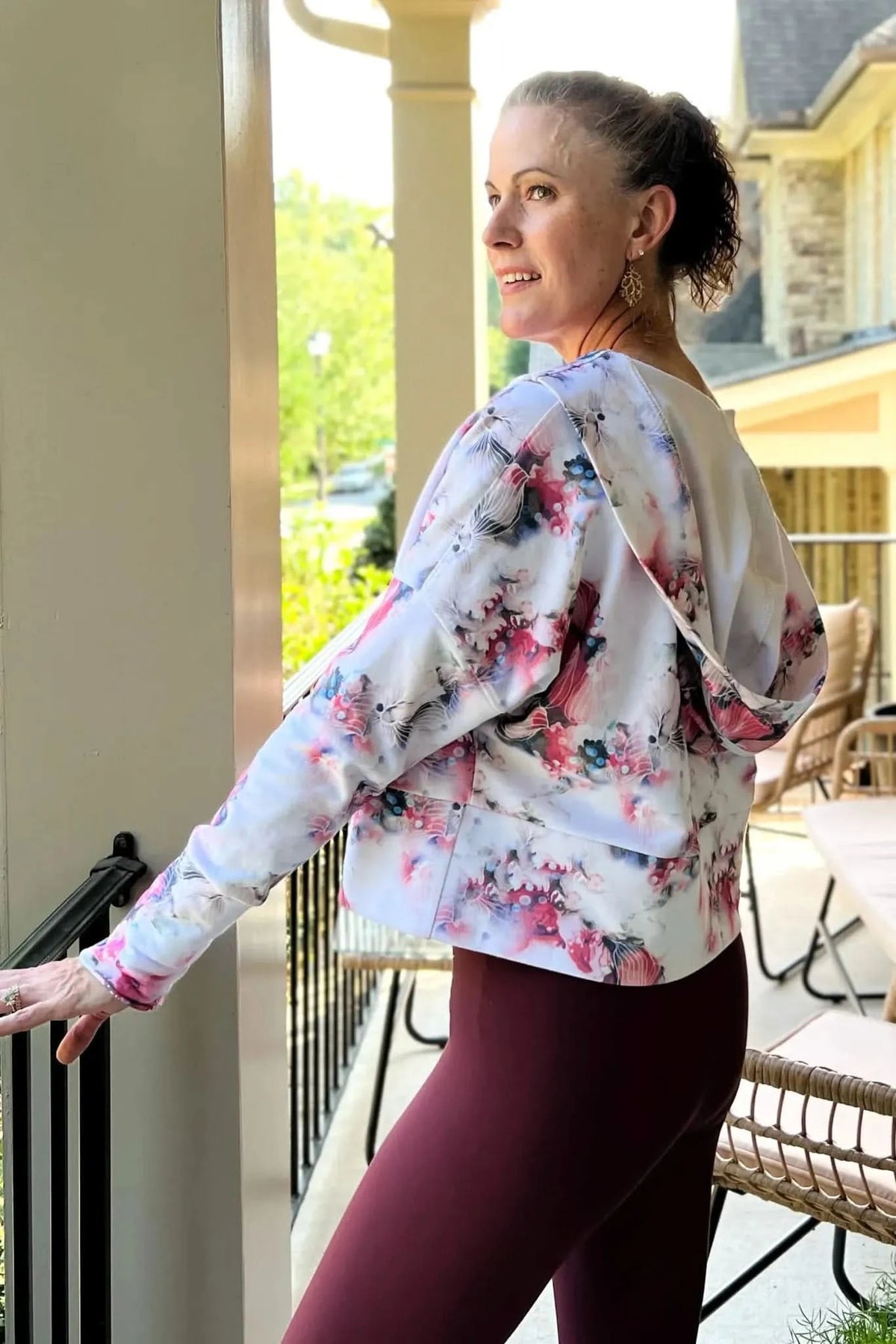 A woman wears a floral hoodie and dark leggings on a porch.