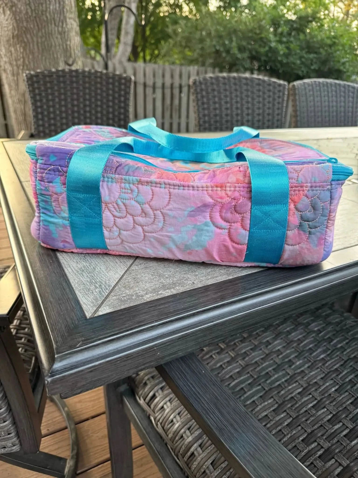 Purple glass flowers fabric with pink and blue accents, shown as a quilted bag on a patio table.