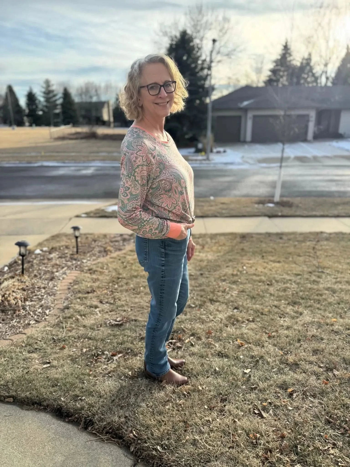 Pink and green paisley maze boho fabric swatch on a woman's sweater and jeans outdoors.