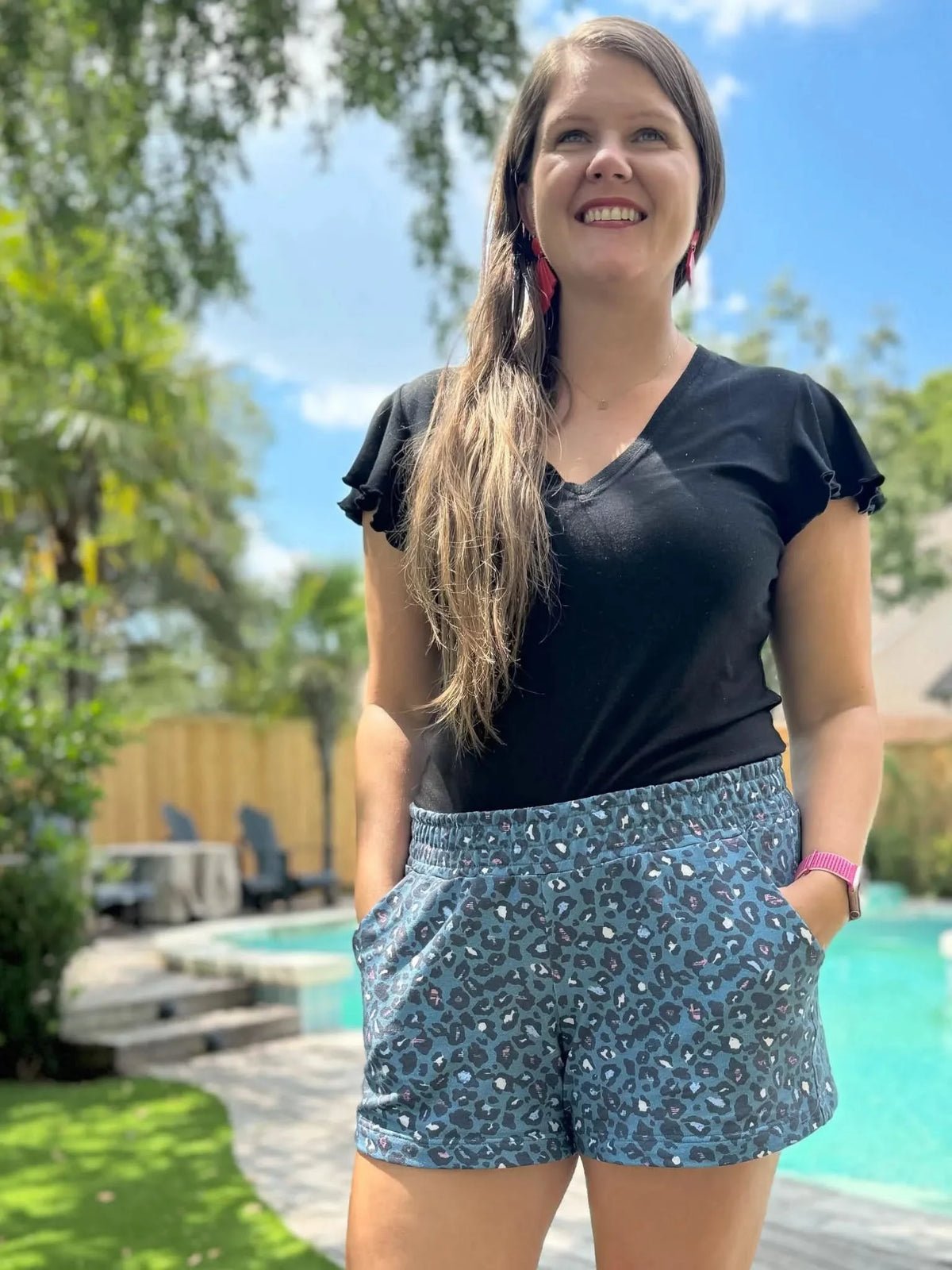 Woman modeling teal leopard print shorts and black flutter-sleeve top outdoors by pool.