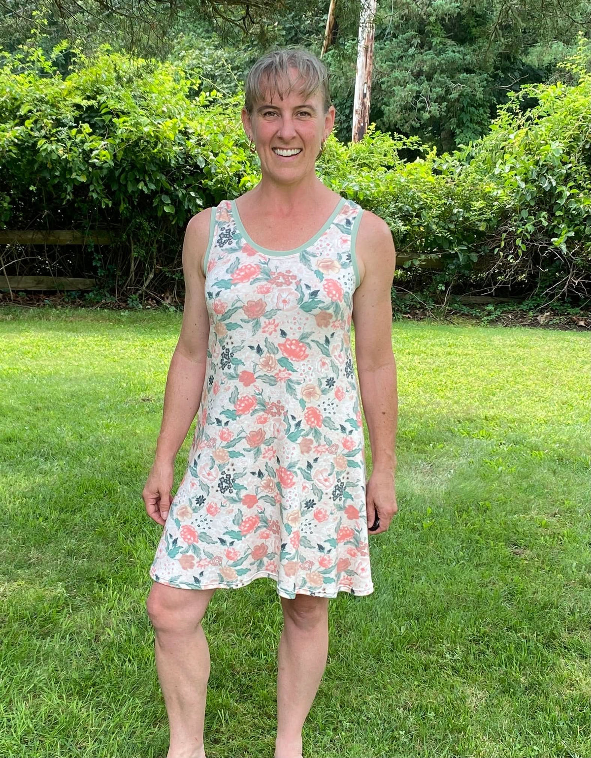 A woman in a floral print dress stands in a grassy yard.
