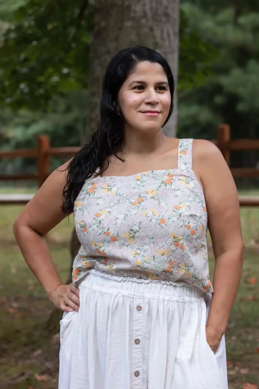 Woman modeling a sleeveless square-neck top in vibrant Moroccan citrus floral print fabric, paired with white button-front pants, standing outdoors.