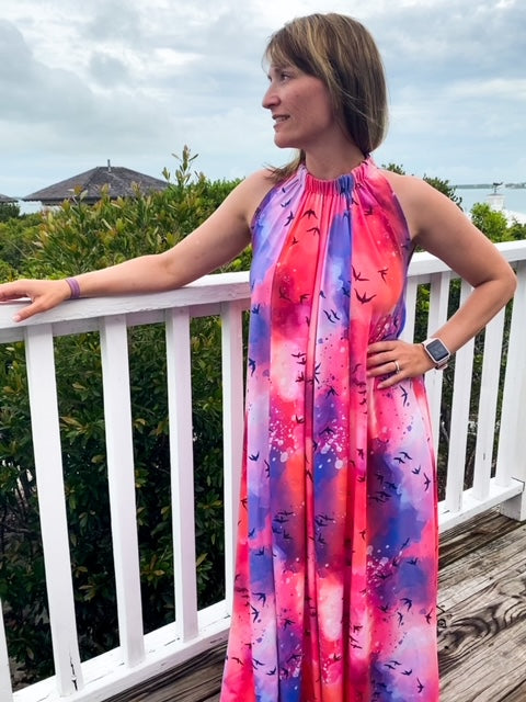 A girl looking down while wearing a pink, red and blue dress with maroon birds on it