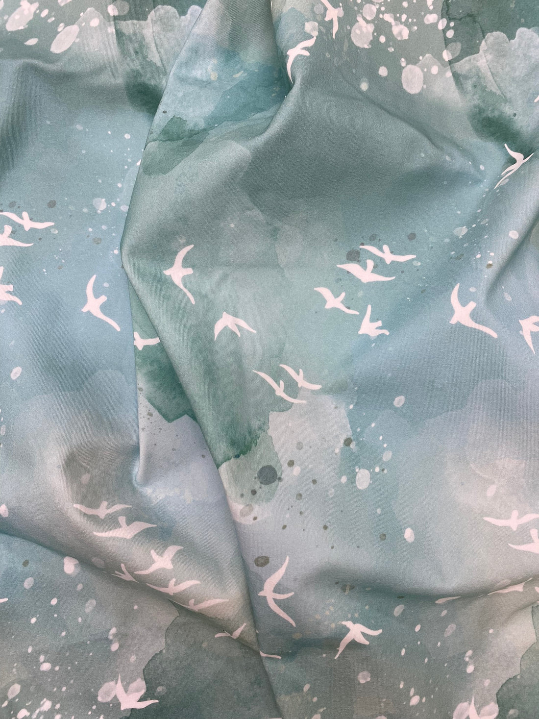 Fabric with green background and white birds flying around