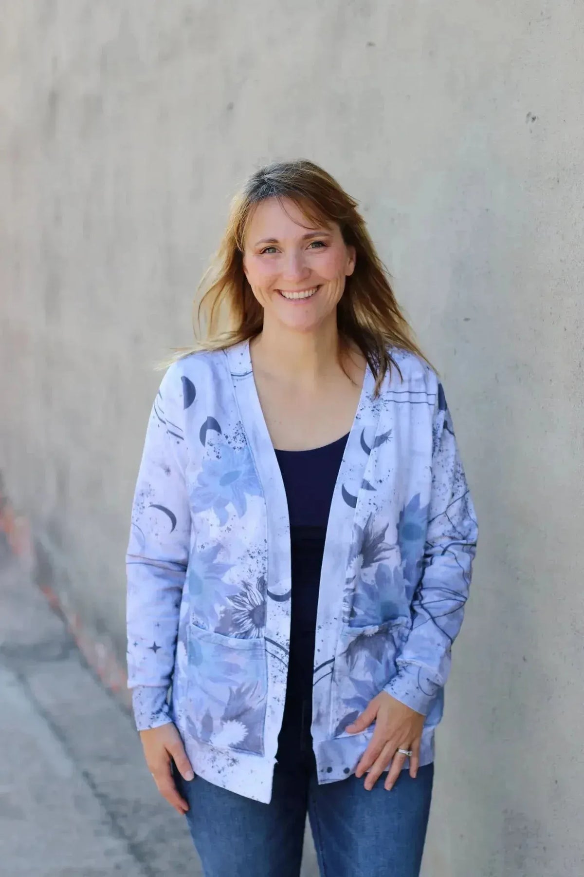 A woman smiles, wearing a blue and white celestial sunflower print cardigan.