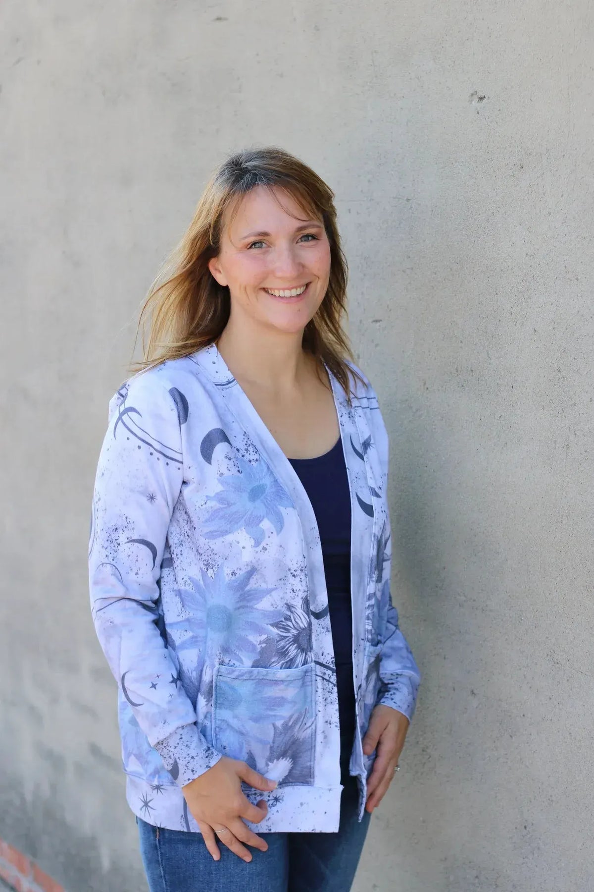 A woman smiles, wearing a light blue cardigan with celestial sunflower patterns.