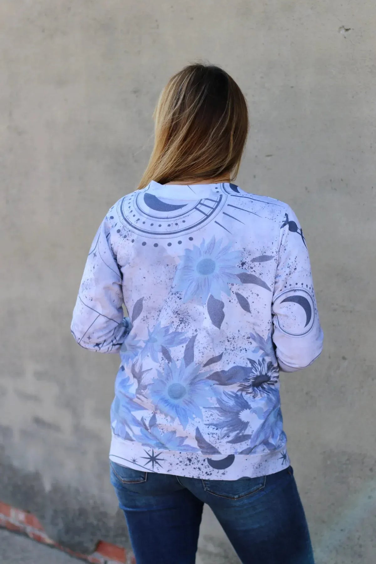 A woman from behind wears a white sweatshirt with blue celestial sunflower print.