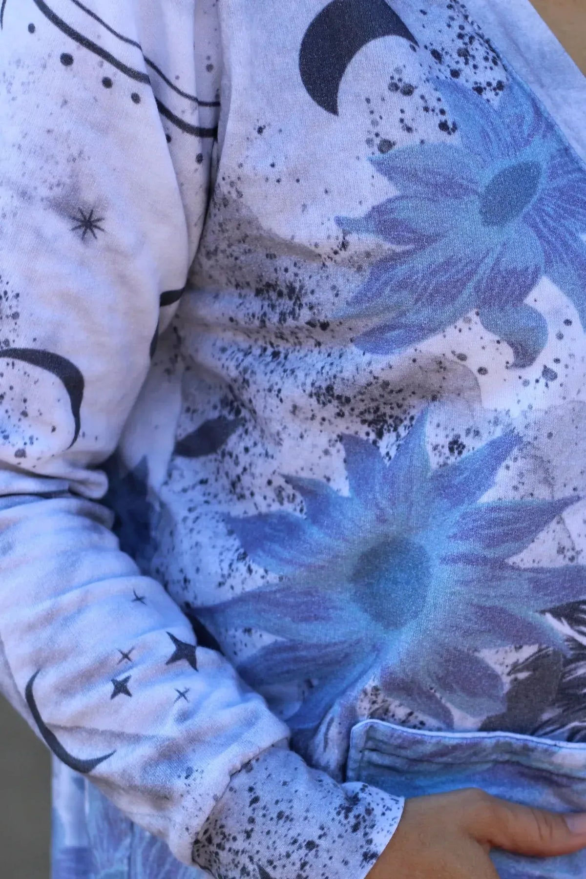 A person wears a garment with blue sunflowers and celestial patterns.