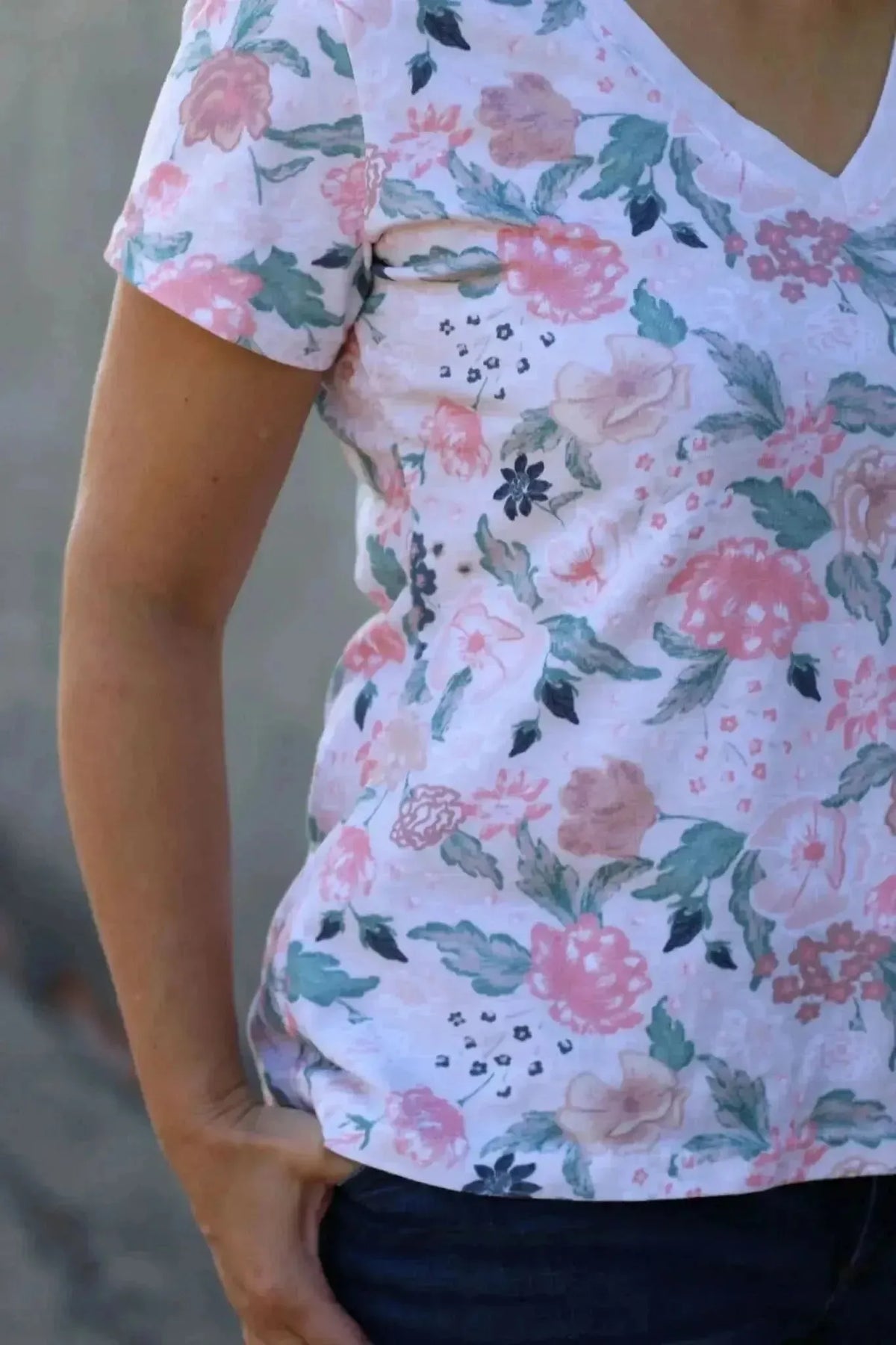 A person wears a white floral top with pink, green, and blue flowers.