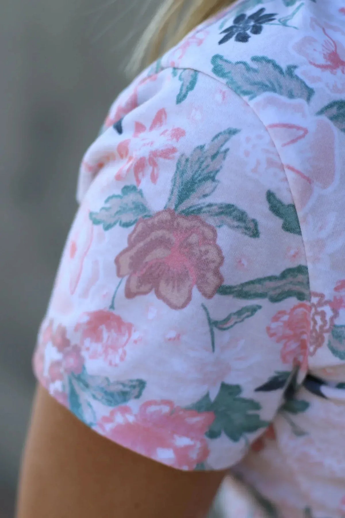A close-up of a person wearing a floral print top with blush and green flowers.