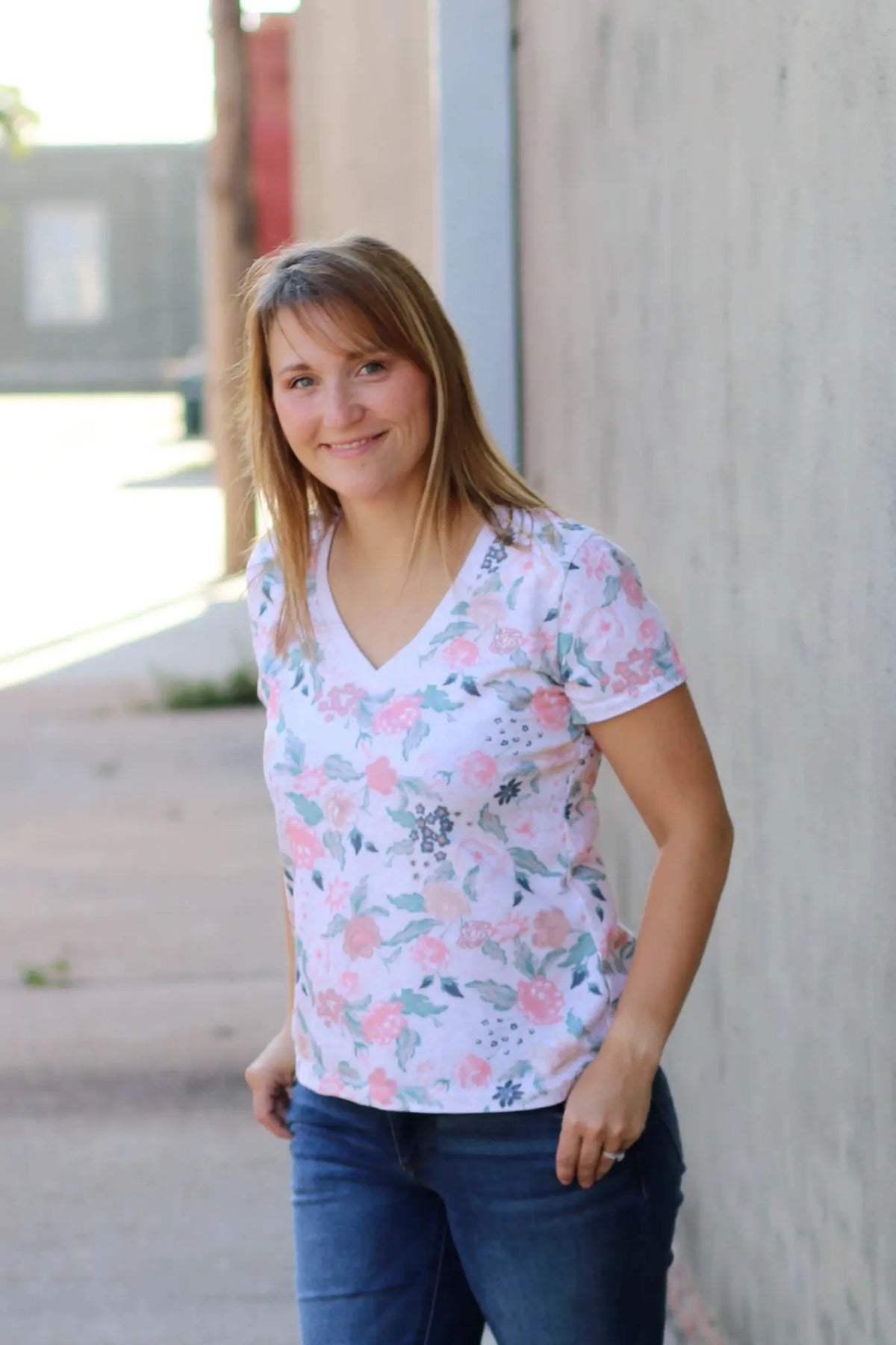 A woman wears a white v-neck shirt with a blush floral pattern and blue jeans.