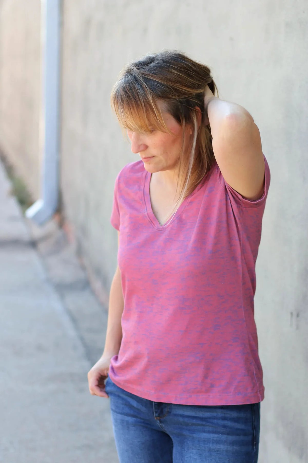 A woman in a pink heather v-neck shirt and jeans looks down.
